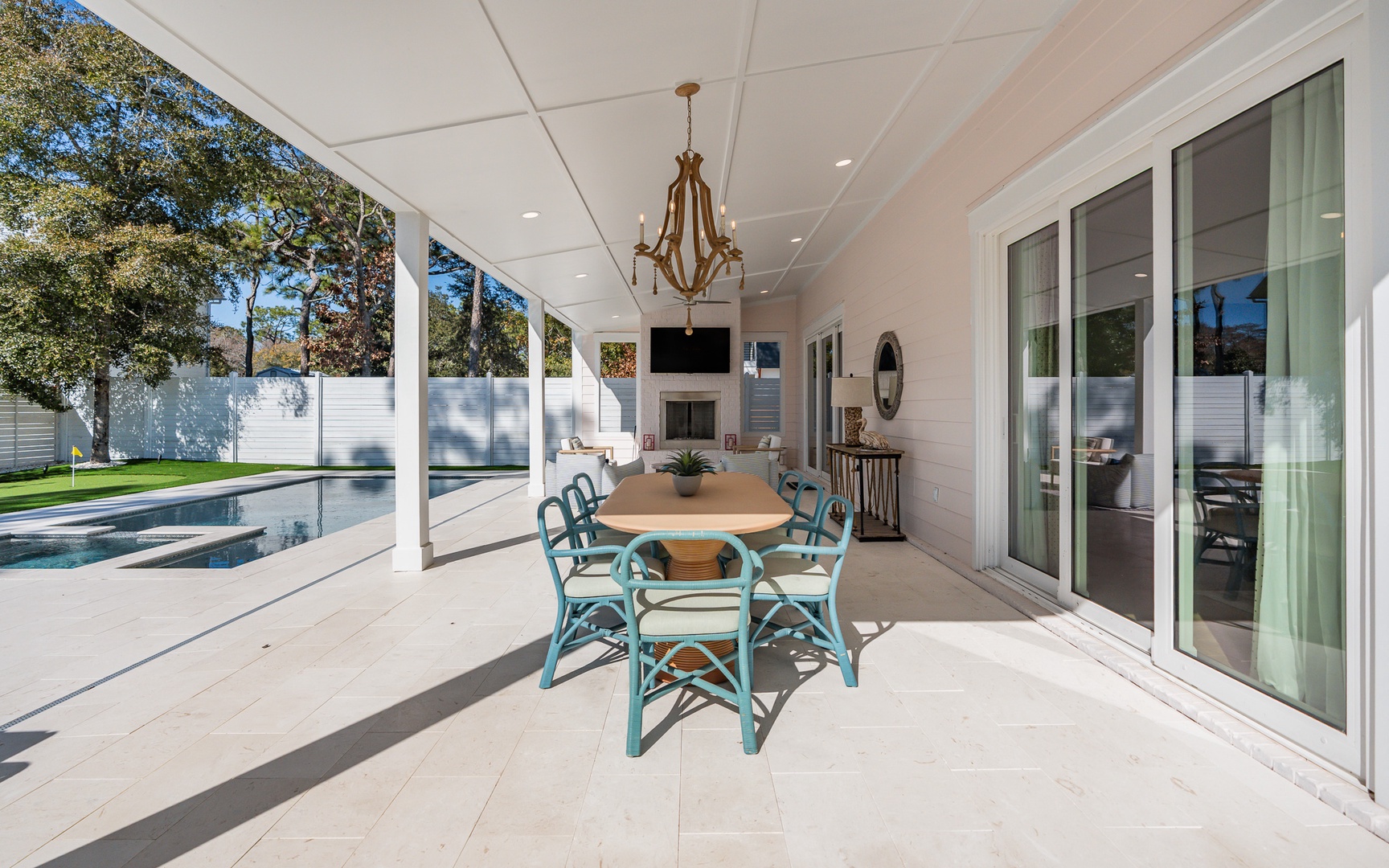 Your elegant covered patio awaits with poolside dining, complete with turquoise chairs and a sparkling chandelier overhead.