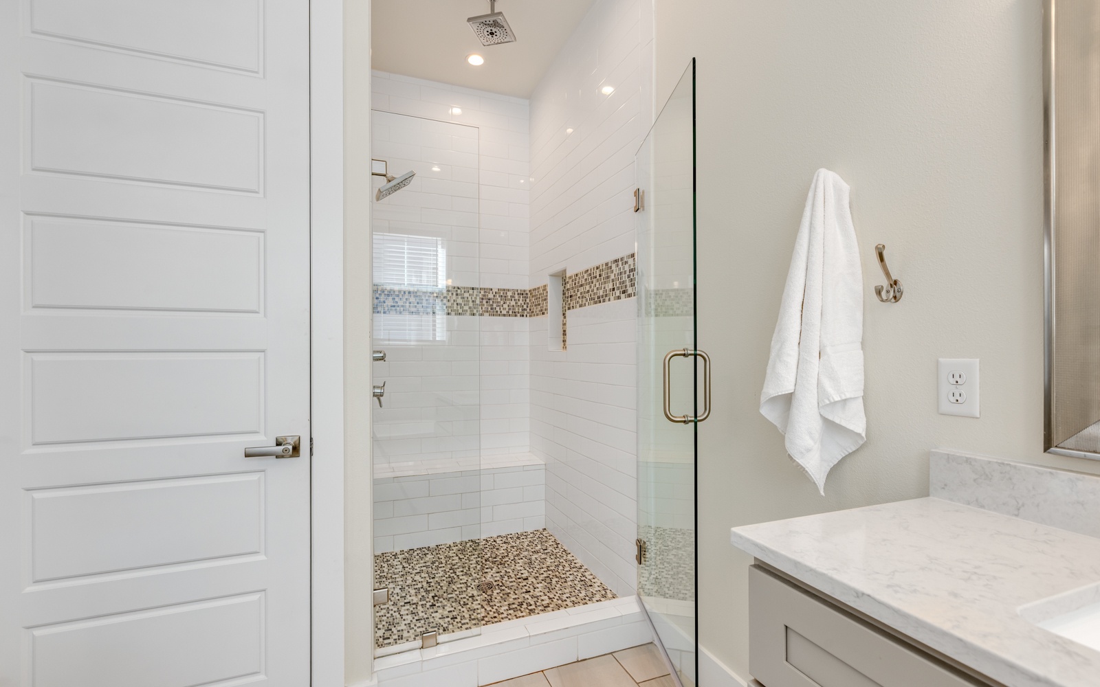 Step into your spa-like bathroom retreat with a stunning glass shower featuring mosaic accents and rainfall showerhead for ultimate relaxation.