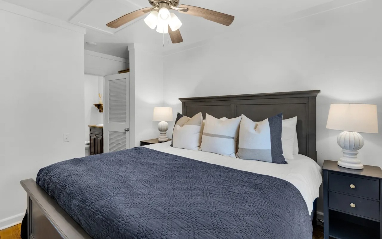 Sink into your cozy sanctuary with crisp white linens, soft navy accents, and gentle ceiling fan breeze for perfect sleep comfort.