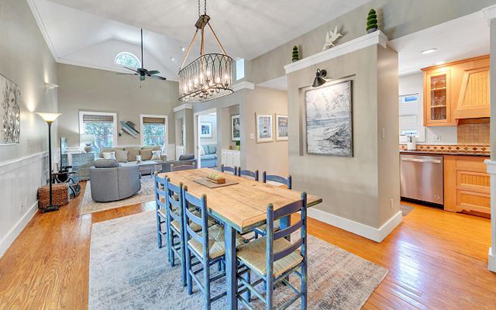 Gather around your spacious dining table where warm wood meets coastal blue chairs under elegant pendant lighting.