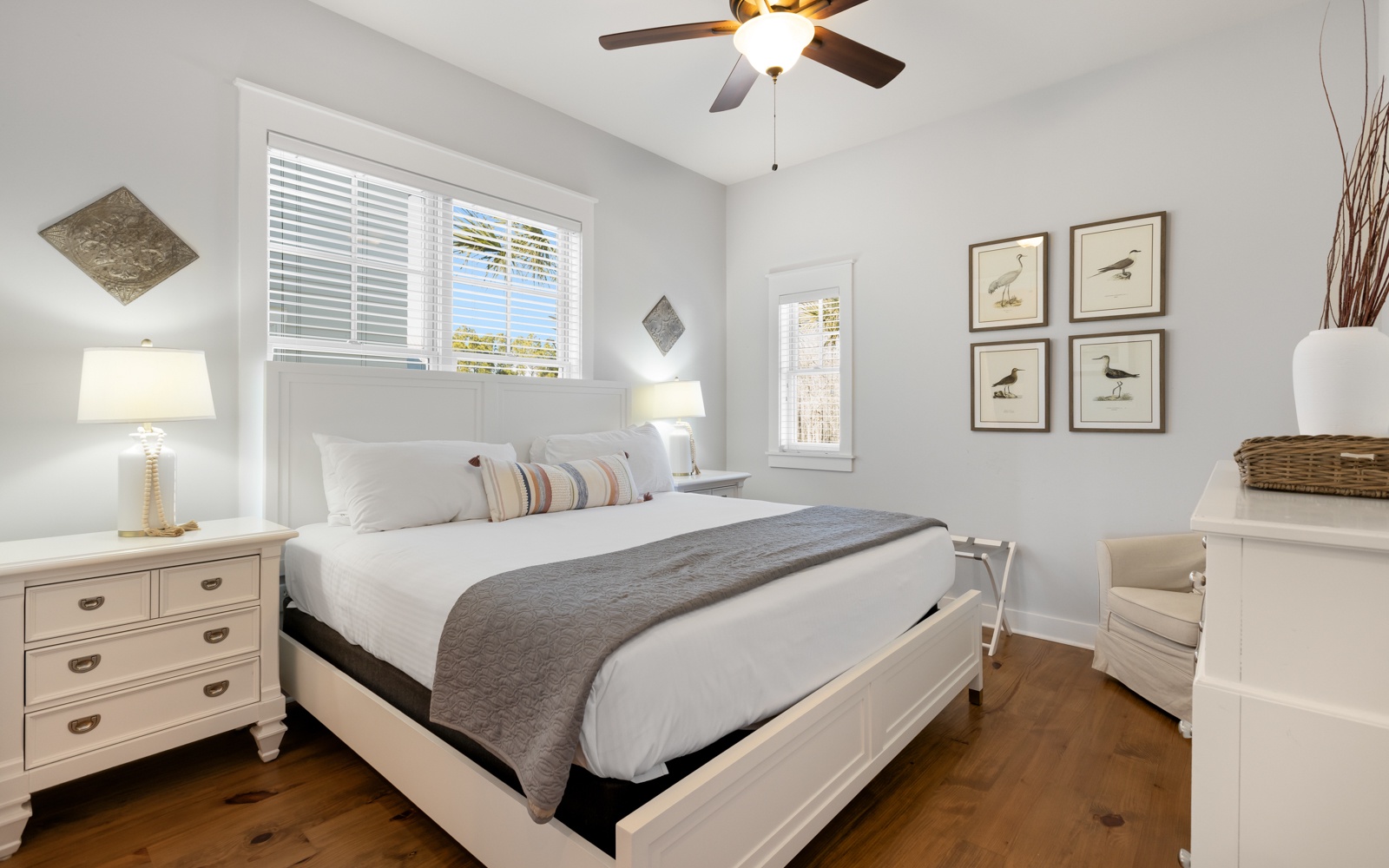 Sink into crisp white linens in your peaceful bedroom, where coastal artwork and gentle ceiling fan breezes create the perfect retreat after your adventures.