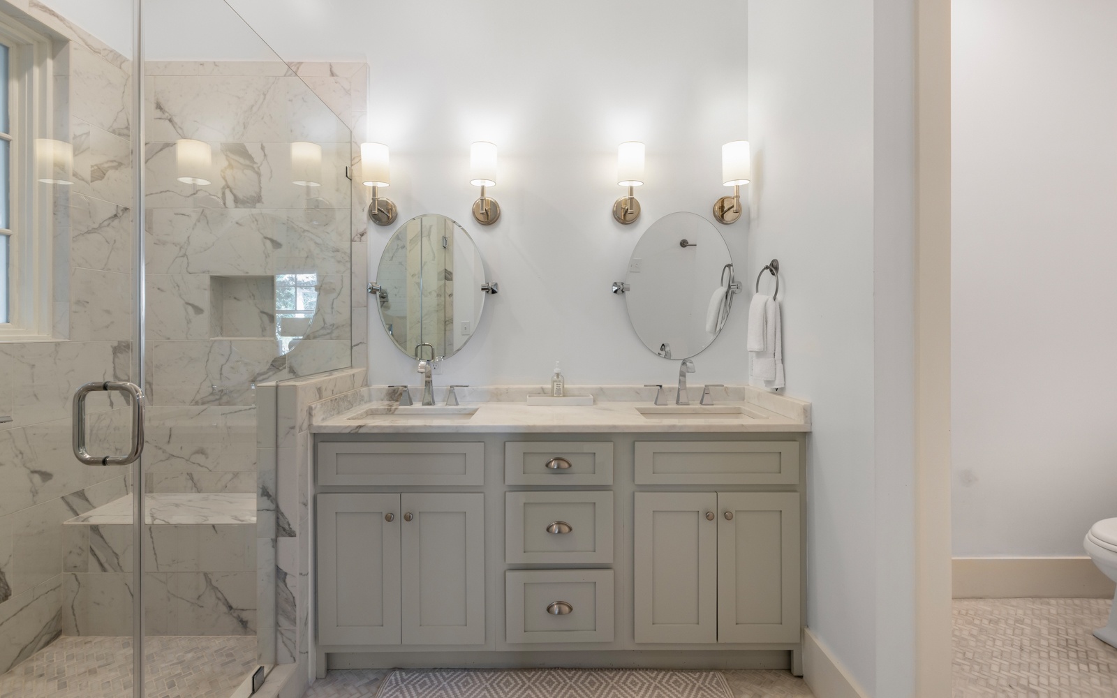 Step into your luxurious marble bathroom featuring dual sinks, elegant brass sconces, and a spacious glass-enclosed shower for ultimate relaxation.