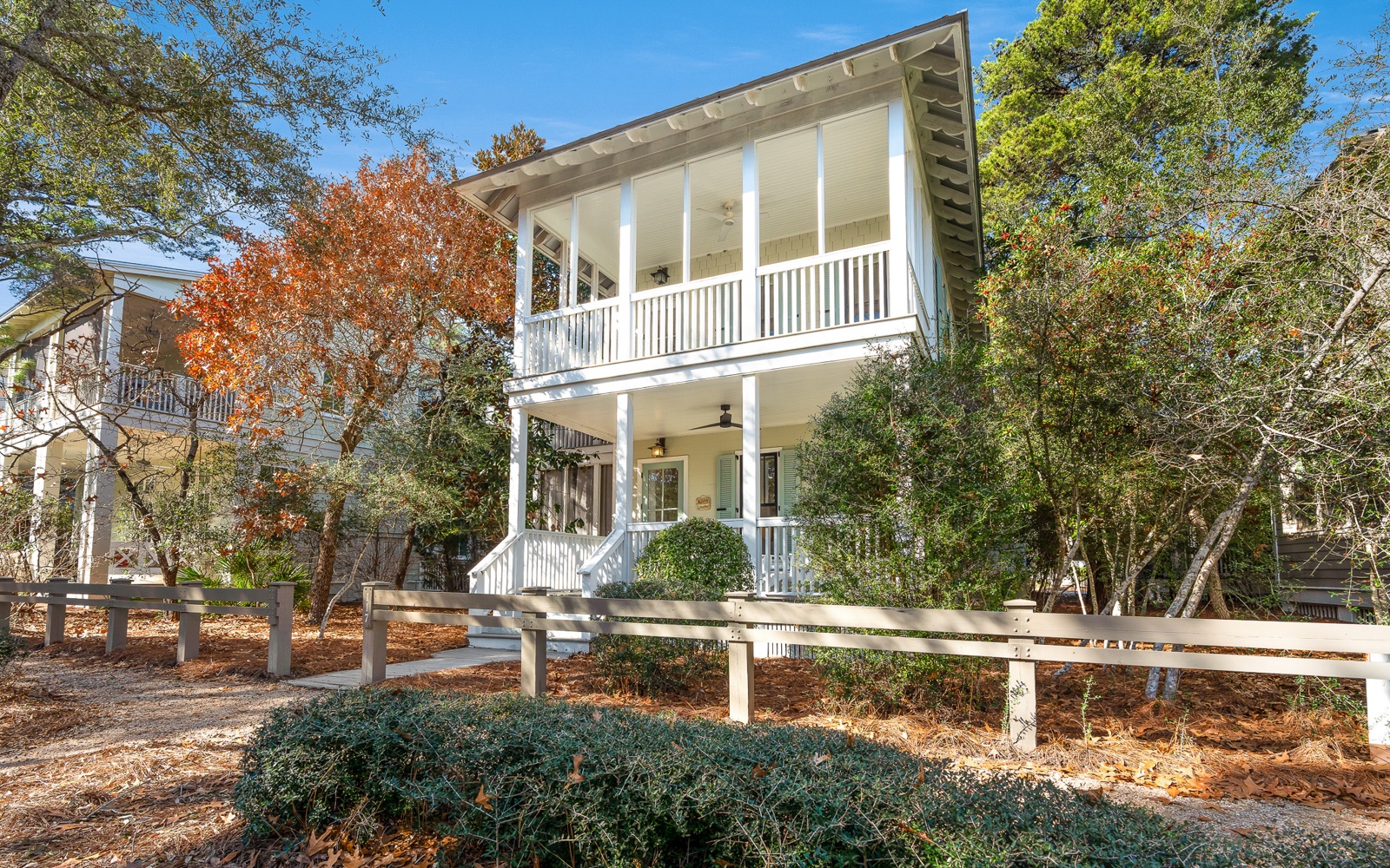 Charming two-story home with wraparound porches nestled among mature trees in a peaceful residential setting.