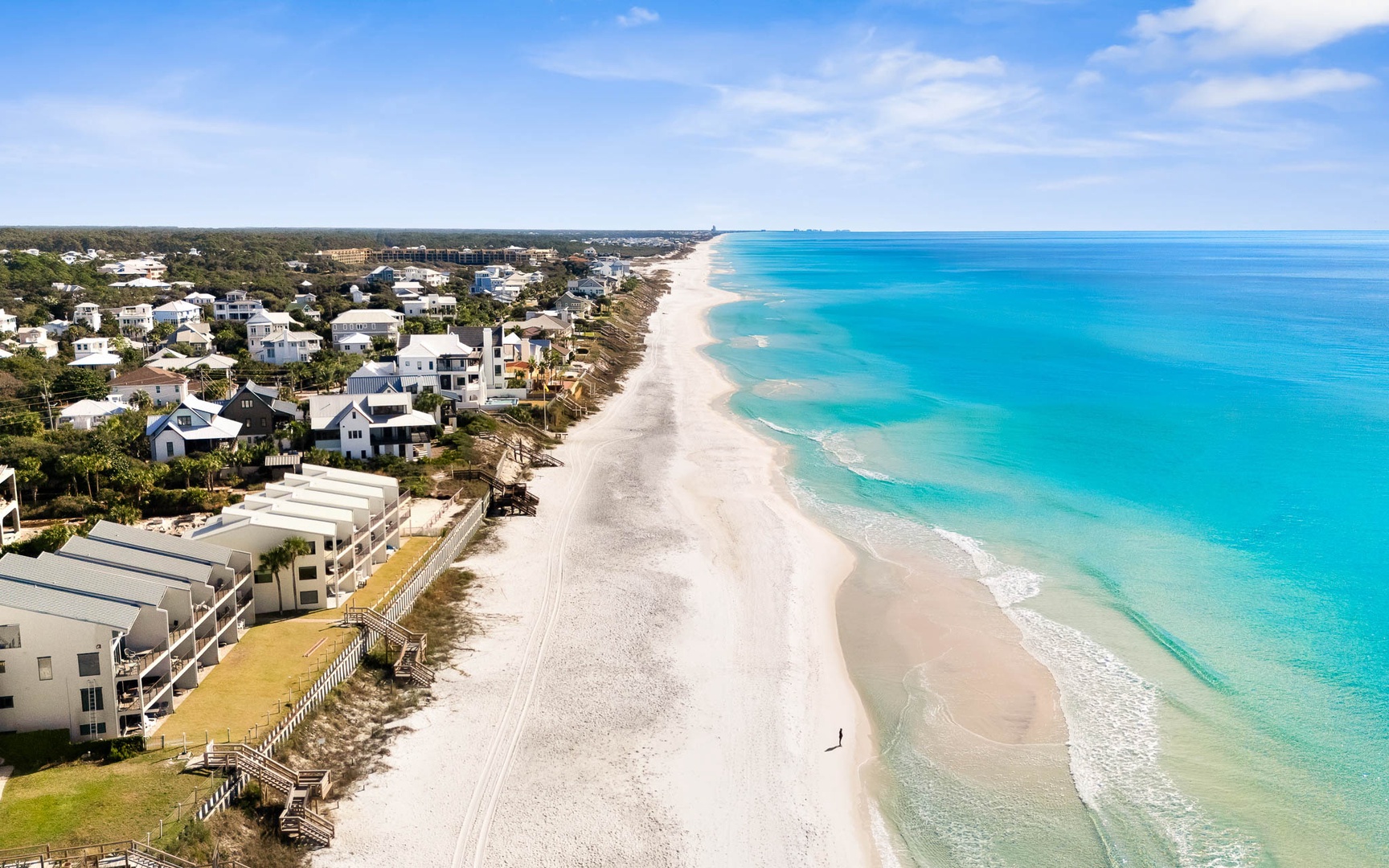Stunning aerial view of pristine white sand beach with crystal-clear turquoise waters stretching along the coastal community.