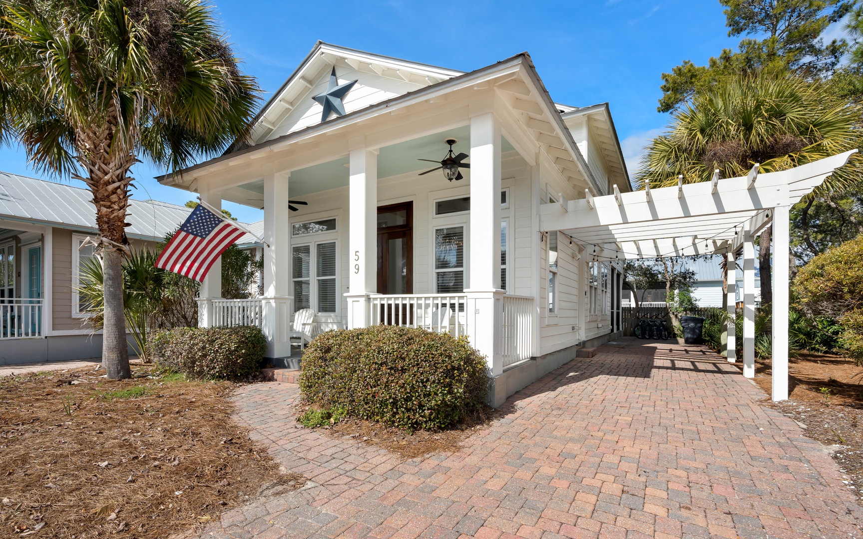 This charming coastal home features classic architecture with white columns and decorative star details, surrounded by tropical palms and mature landscaping.