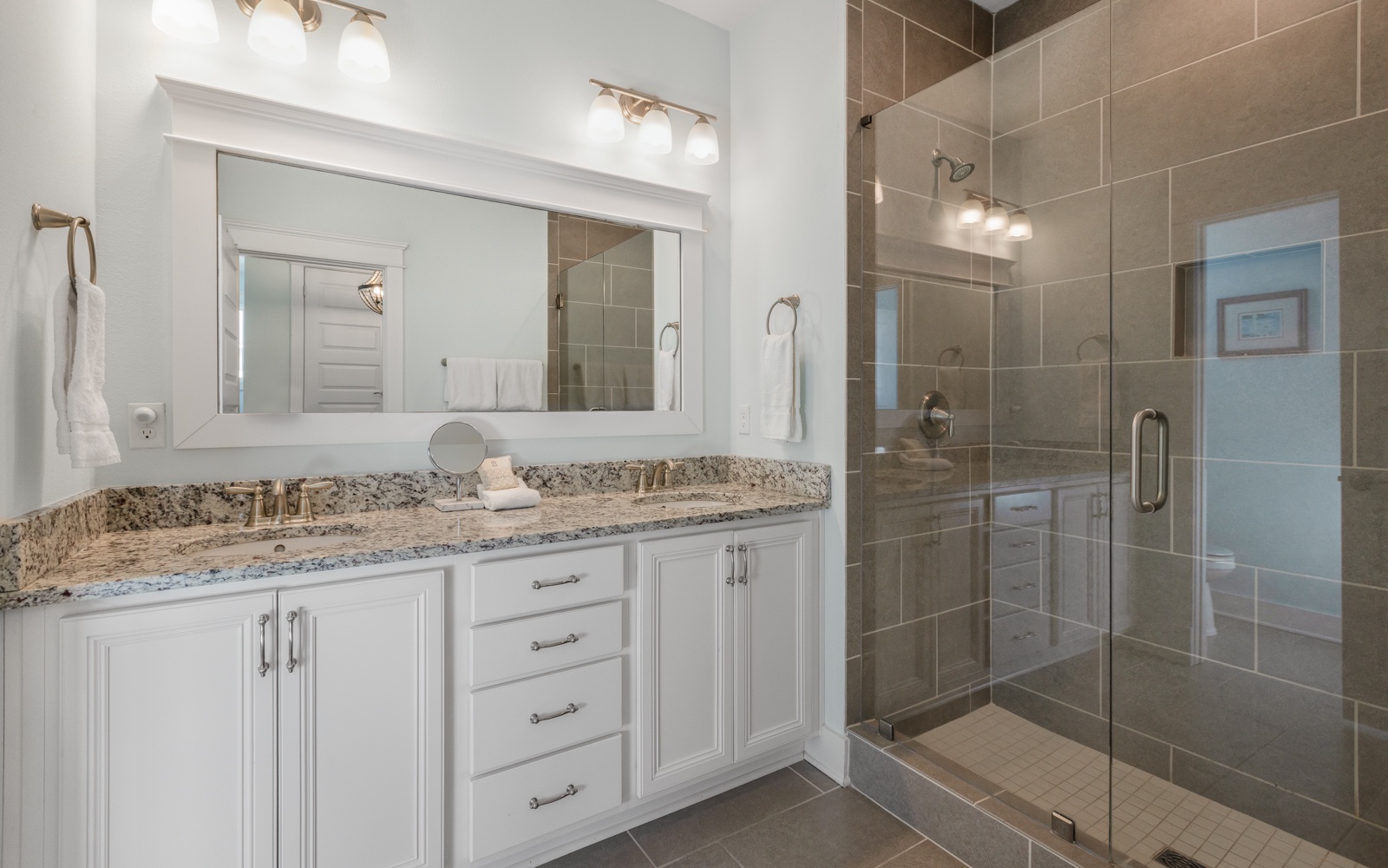 Your spacious bathroom features elegant granite countertops, bright vanity lighting, and a luxurious glass-enclosed shower for ultimate relaxation.