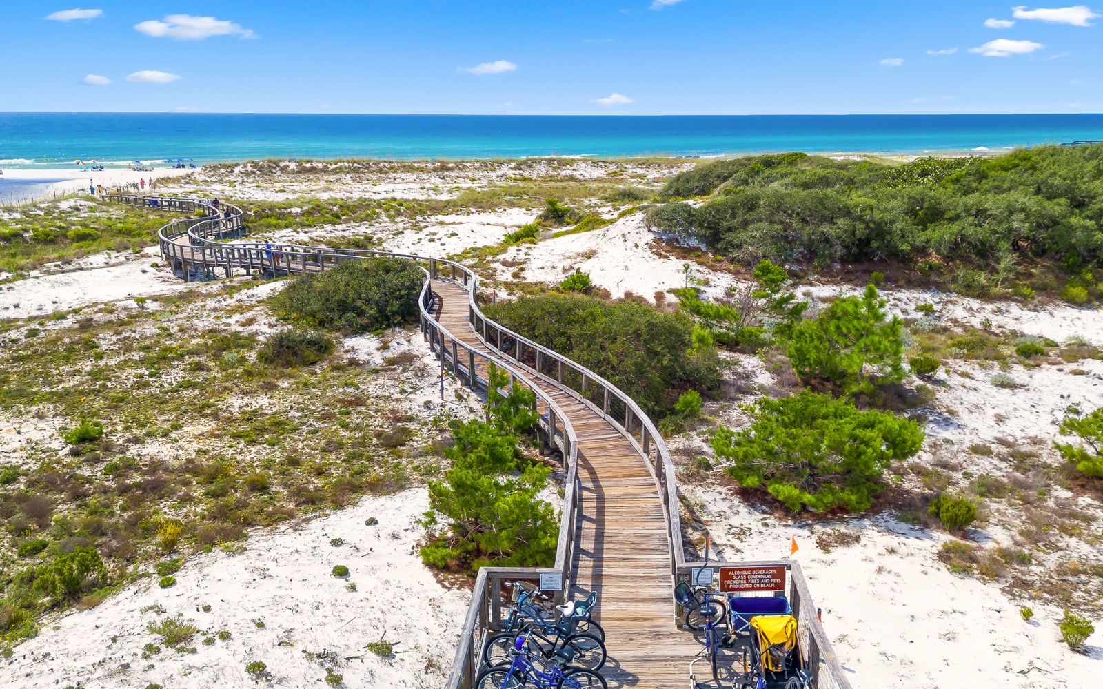 Elevated wooden boardwalk winds through protected coastal dunes toward pristine beach access.