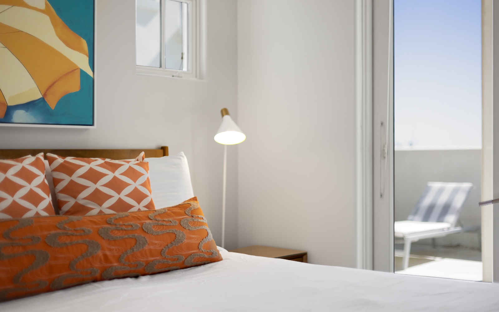 Sink into crisp linens and vibrant pillows as warm light creates your perfect reading nook with balcony access.