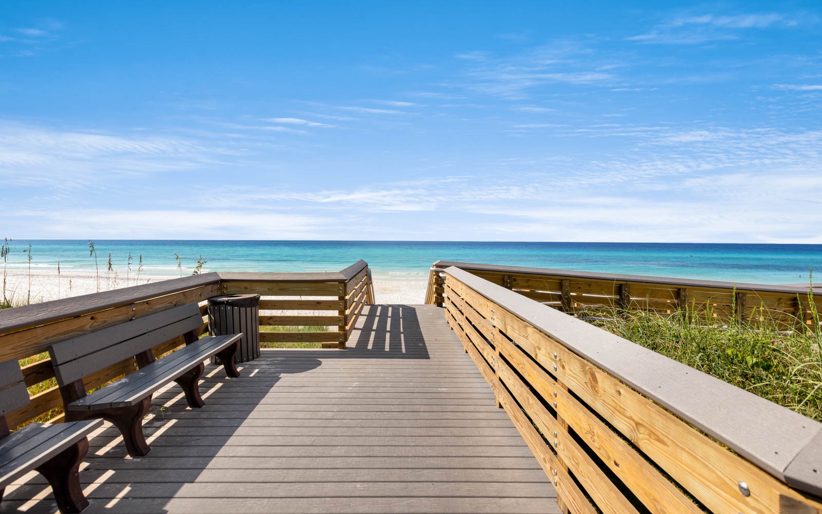 Wooden boardwalk overlooking pristine white sand beach and turquoise waters under clear blue skies.