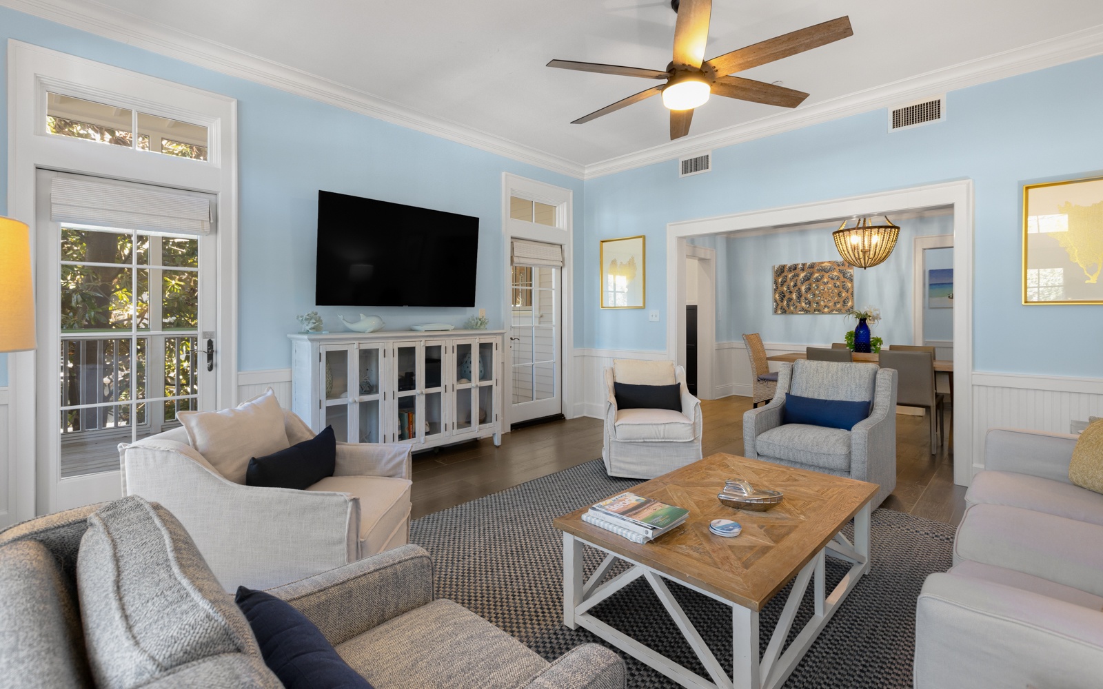 Relax in your stylish living room featuring cozy seating, a large TV, and gentle ceiling fan breeze flowing through French doors.