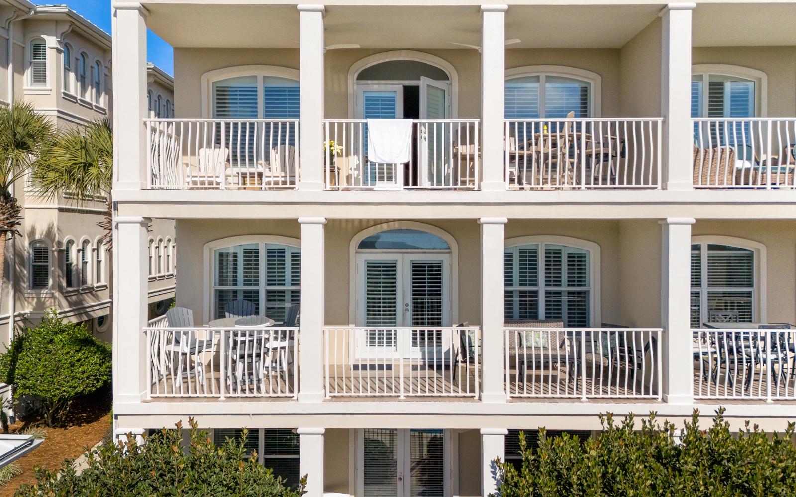 Elegant coastal architecture featuring multiple private balconies with white railings and arched windows in a peaceful beachside setting.