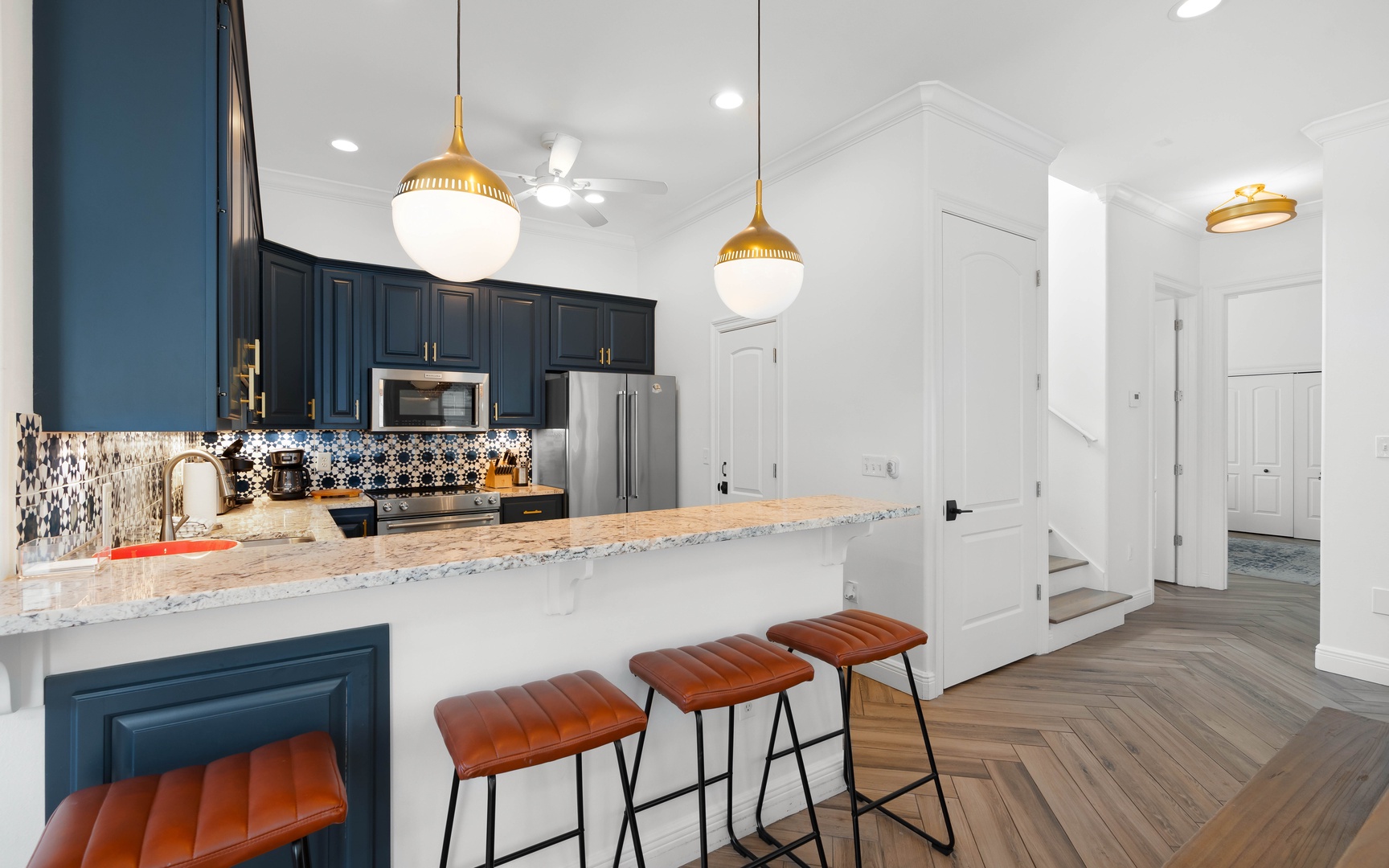 You'll love cooking in this stylish kitchen featuring navy cabinets, gold pendant lights, and a spacious marble island perfect for morning coffee.