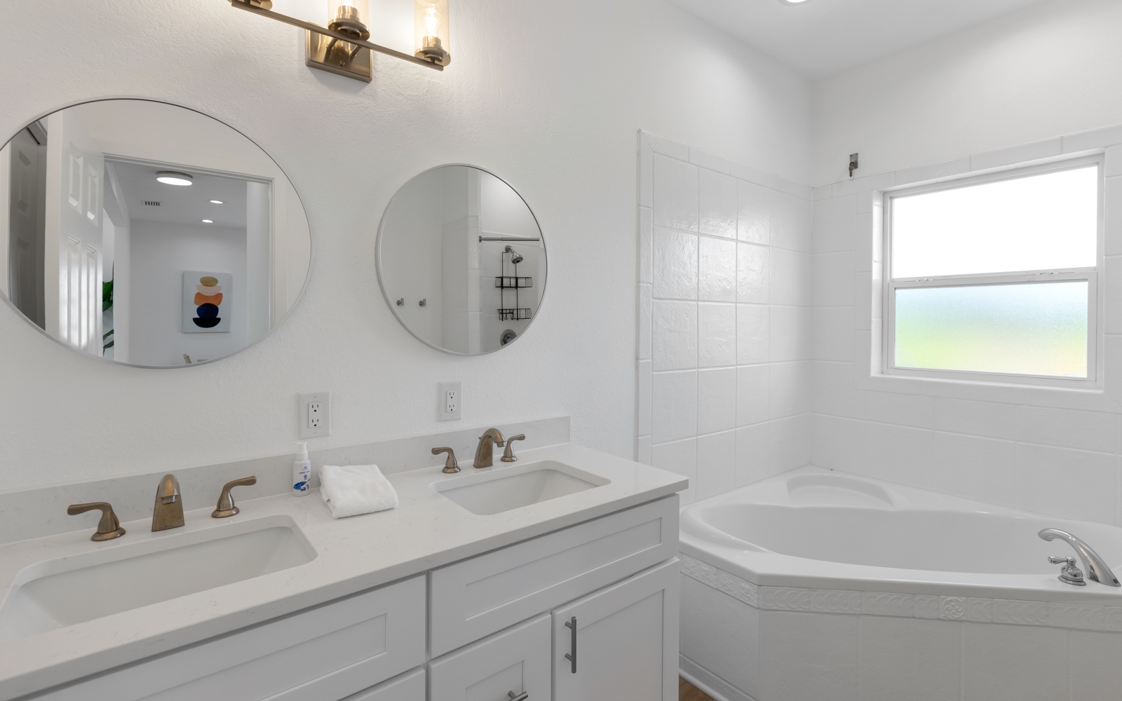 Unwind in your pristine bathroom with dual vanities, soaking tub, and natural light streaming through the window.