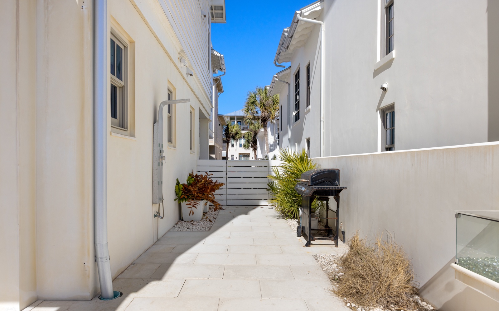 Charming white-washed buildings frame this peaceful residential street, featuring tropical landscaping and clear blue skies overhead.