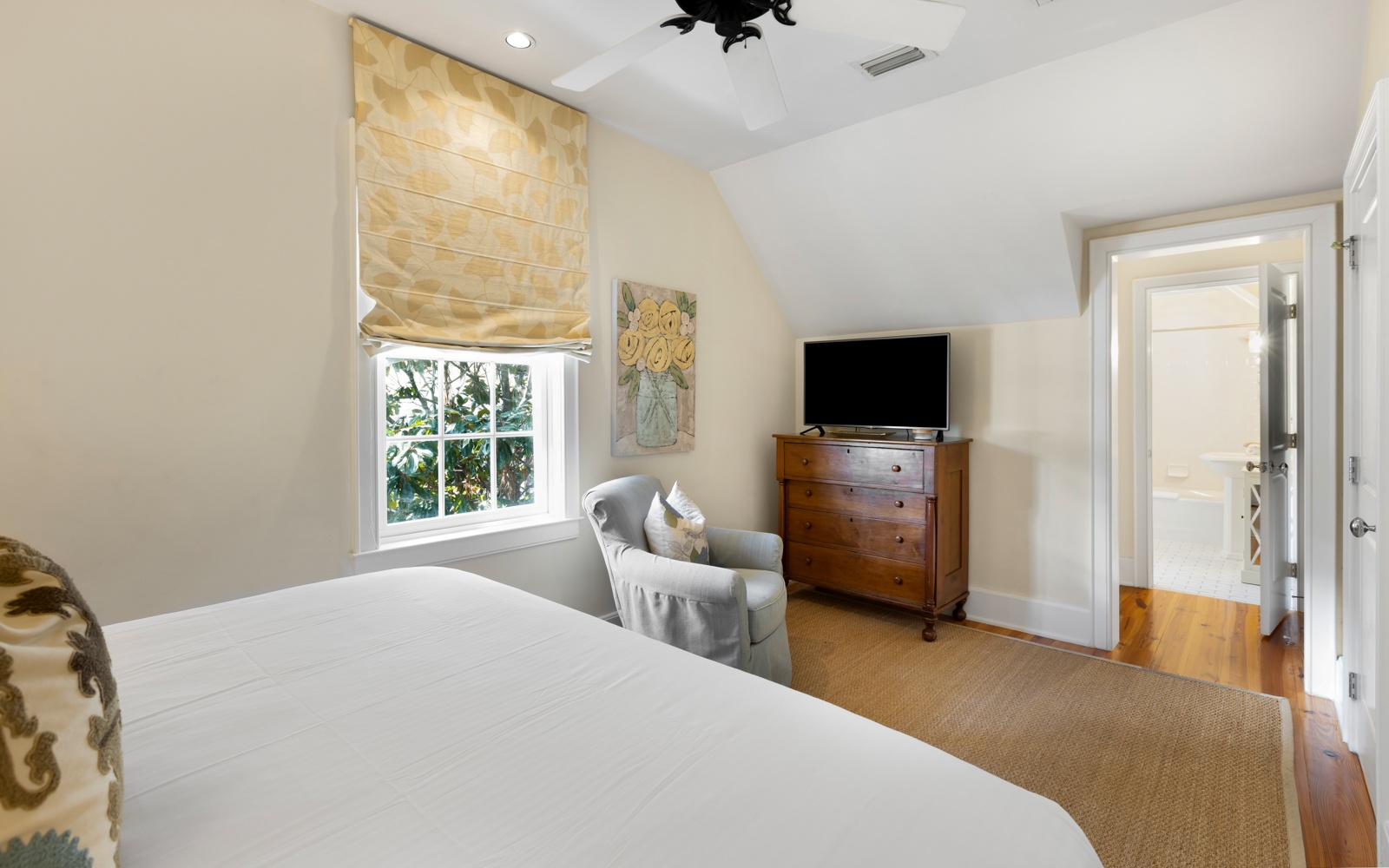 Unwind in your peaceful bedroom featuring a plush reading chair, warm natural light, and entertainment center for cozy evenings.