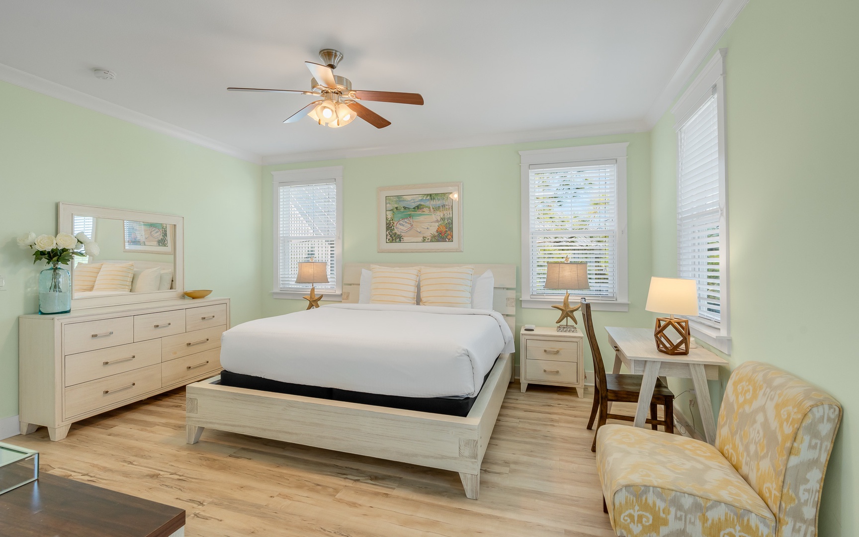 Relax in your coastal bedroom with calming green walls, crisp linens, and gentle ceiling fan breezes.