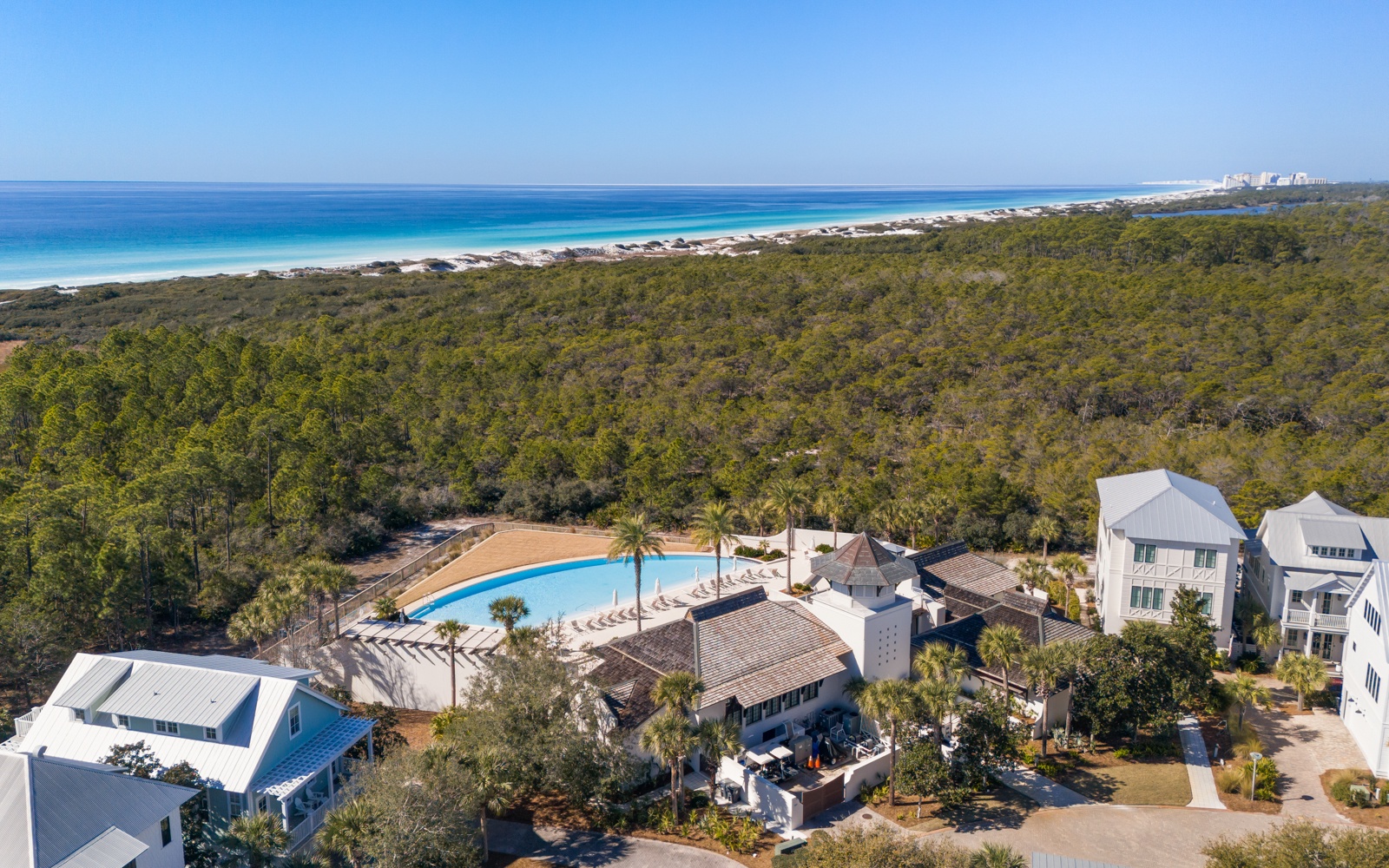 Stunning aerial view of vacation properties nestled between lush forest and pristine white sand beaches with crystal-clear turquoise waters.