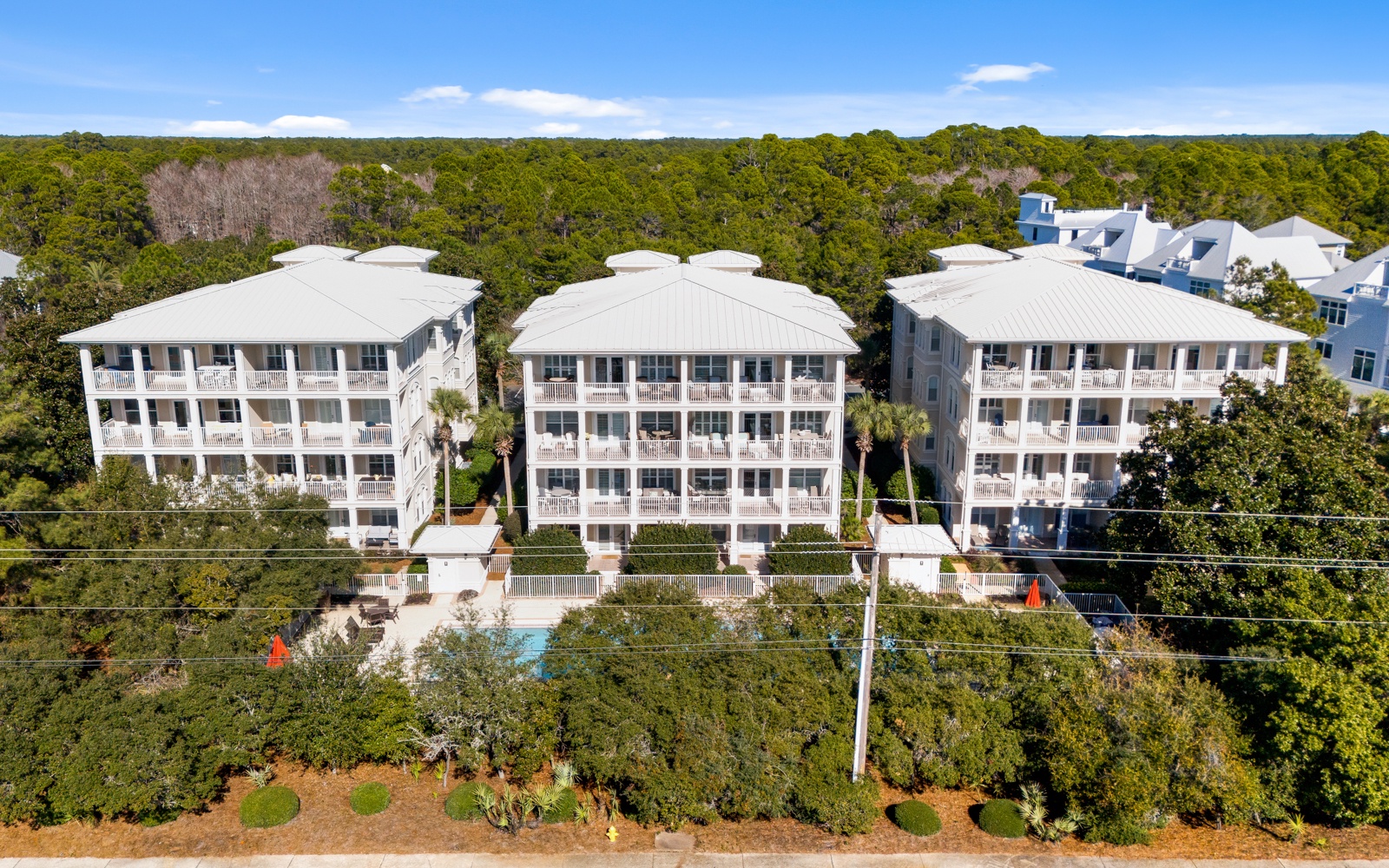 Elegant coastal resort buildings nestled among lush forest canopy, featuring white architecture with private balconies and pool amenities.