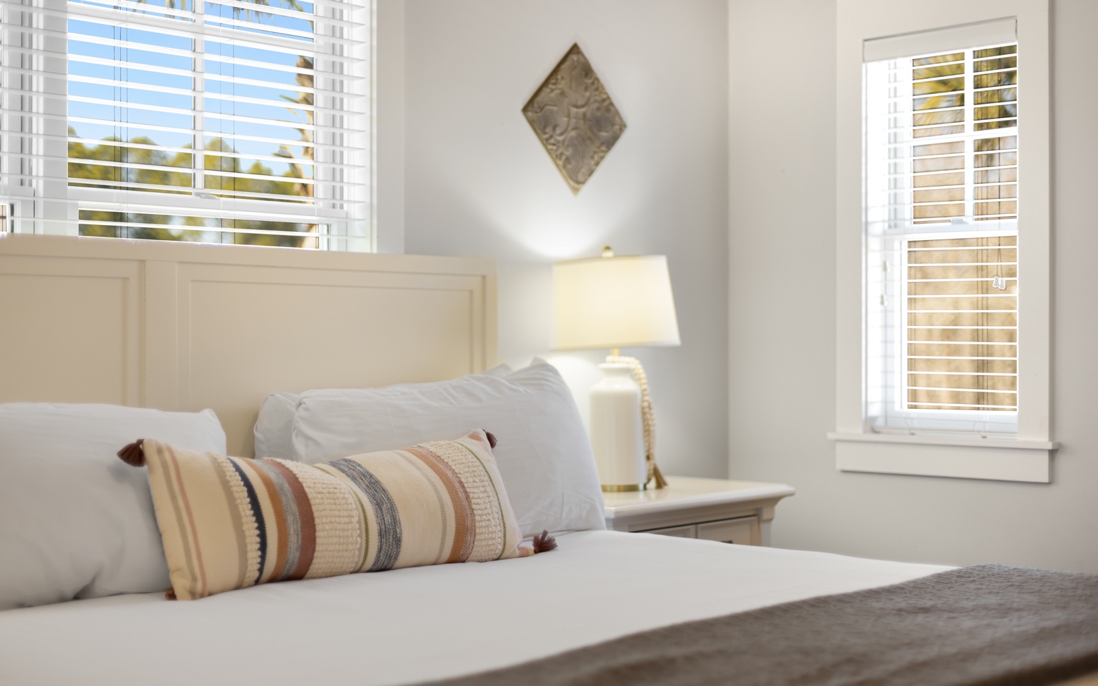 Sink into crisp white linens and plush pillows in your bright, serene bedroom where natural light streams through plantation shutters.