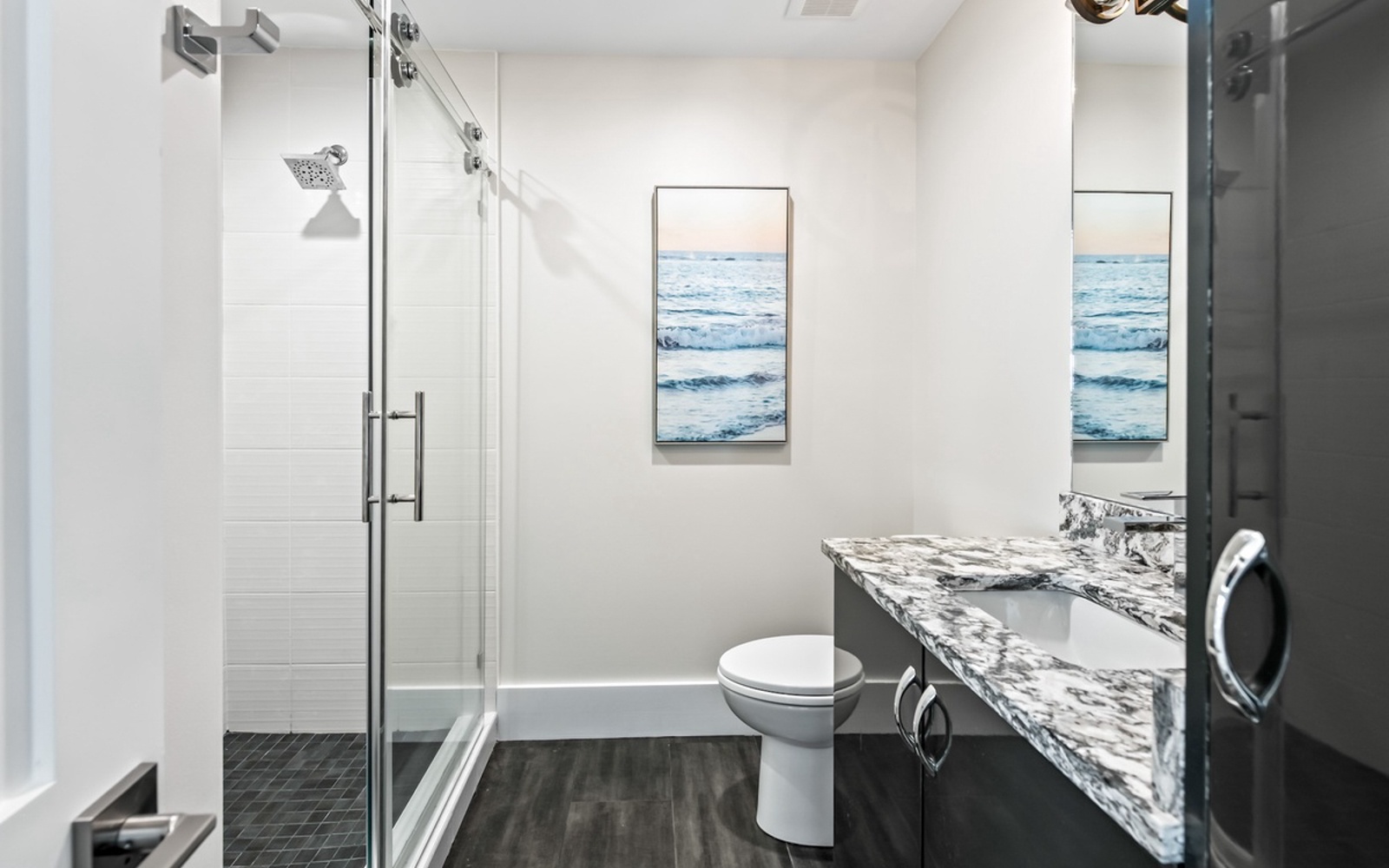 Refresh in your sleek bathroom featuring a spacious glass shower, elegant marble vanity, and coastal artwork creating a spa-like retreat.