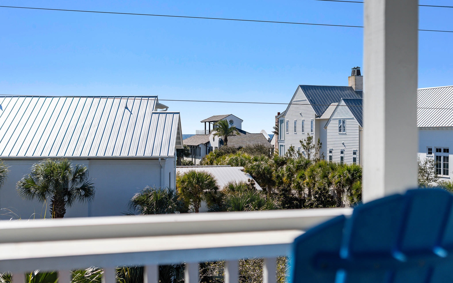 Charming coastal neighborhood with traditional homes featuring metal roofing and tropical palm landscaping under clear blue skies.