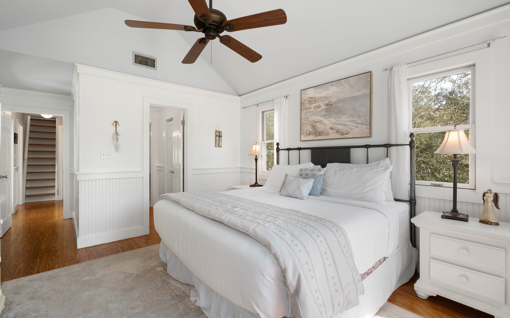 Unwind in your peaceful bedroom featuring crisp white linens, warm wood floors, and a gentle ceiling fan overhead.