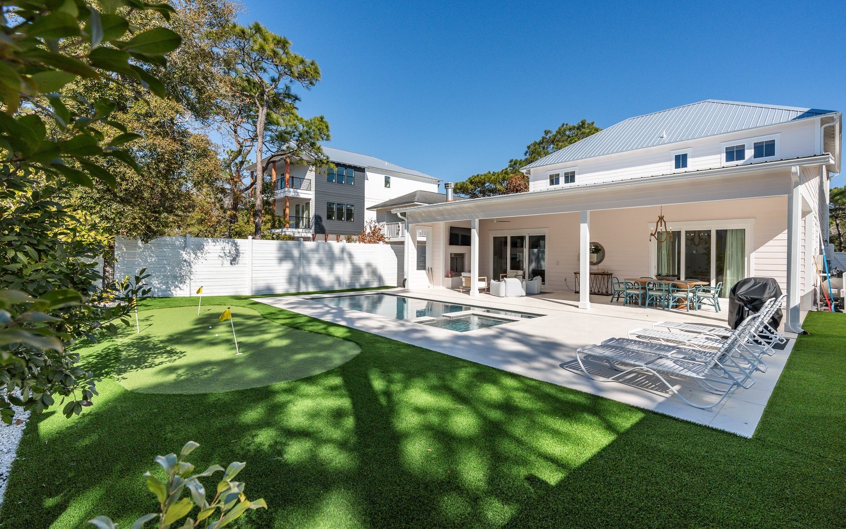 Modern vacation rental with swimming pool and covered patio area surrounded by lush landscaping and mature trees.