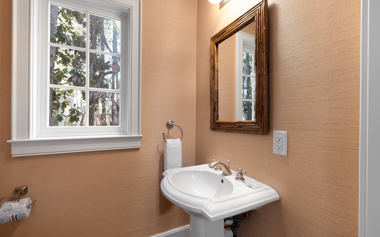 Freshen up in your elegant powder room featuring a classic pedestal sink, warm natural lighting, and charming garden views.