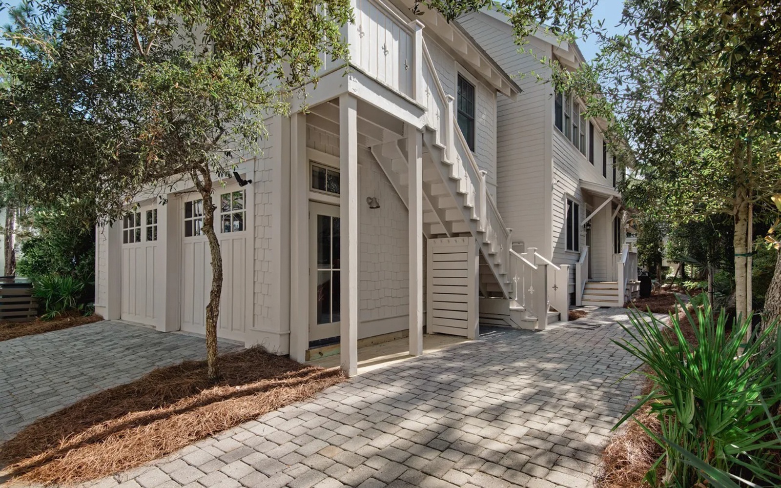 Charming coastal-style home with elegant exterior staircase and mature landscaping in a peaceful residential setting.