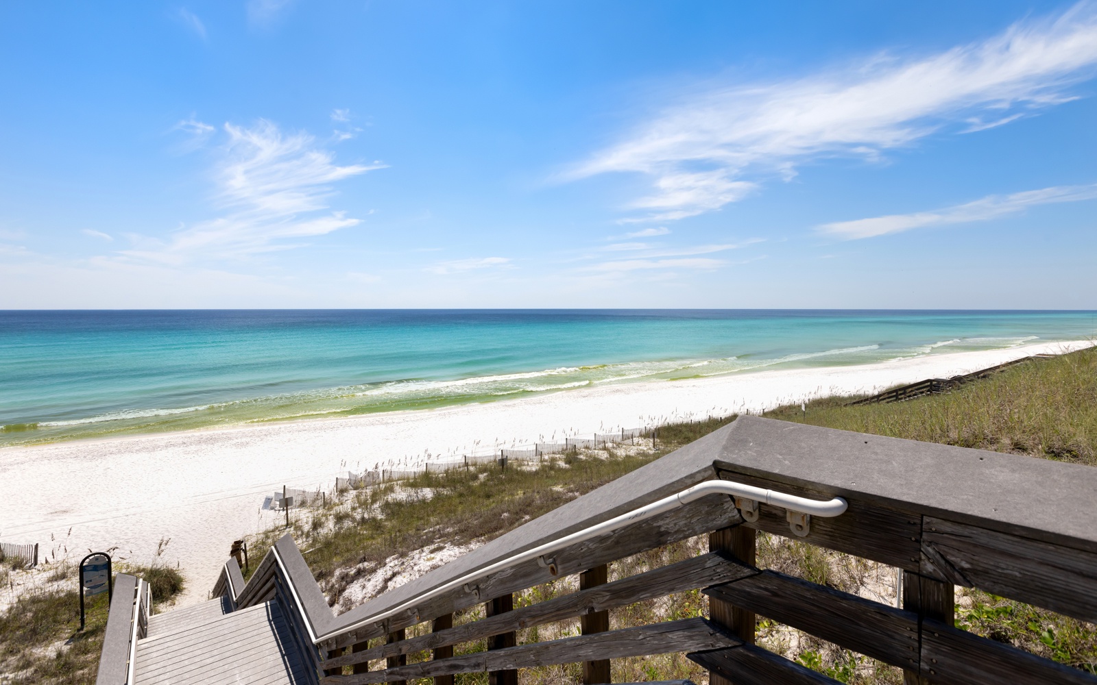 Pristine white sand beach with crystal-clear turquoise waters stretches along the coastline under a brilliant blue sky.