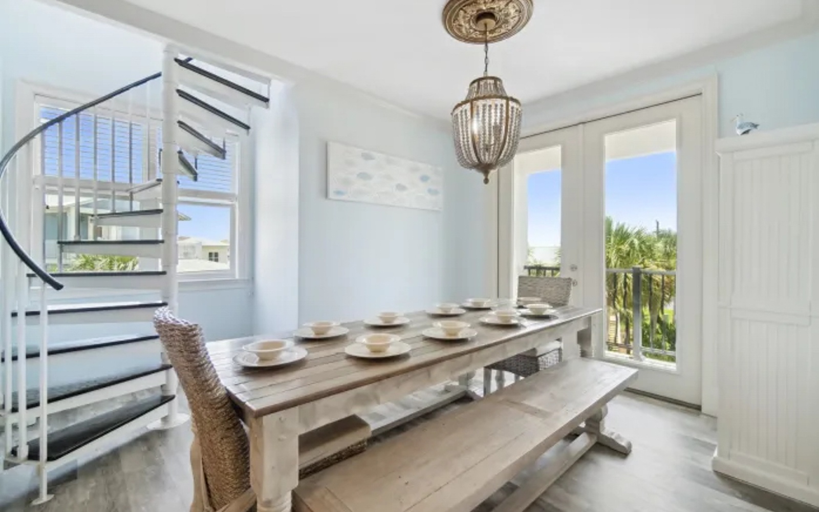 Your bright dining space features a stunning rustic table beneath an elegant chandelier, with French doors opening to tropical views.