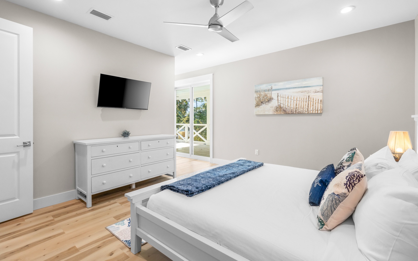 Drift off in this serene coastal bedroom with crisp linens, warm wood floors, and gentle ocean breezes from your private balcony.