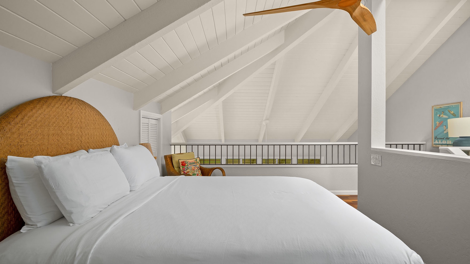 Drift off beneath vaulted ceilings in this cozy loft bedroom, where crisp white linens and a woven rattan headboard create your perfect coastal retreat.