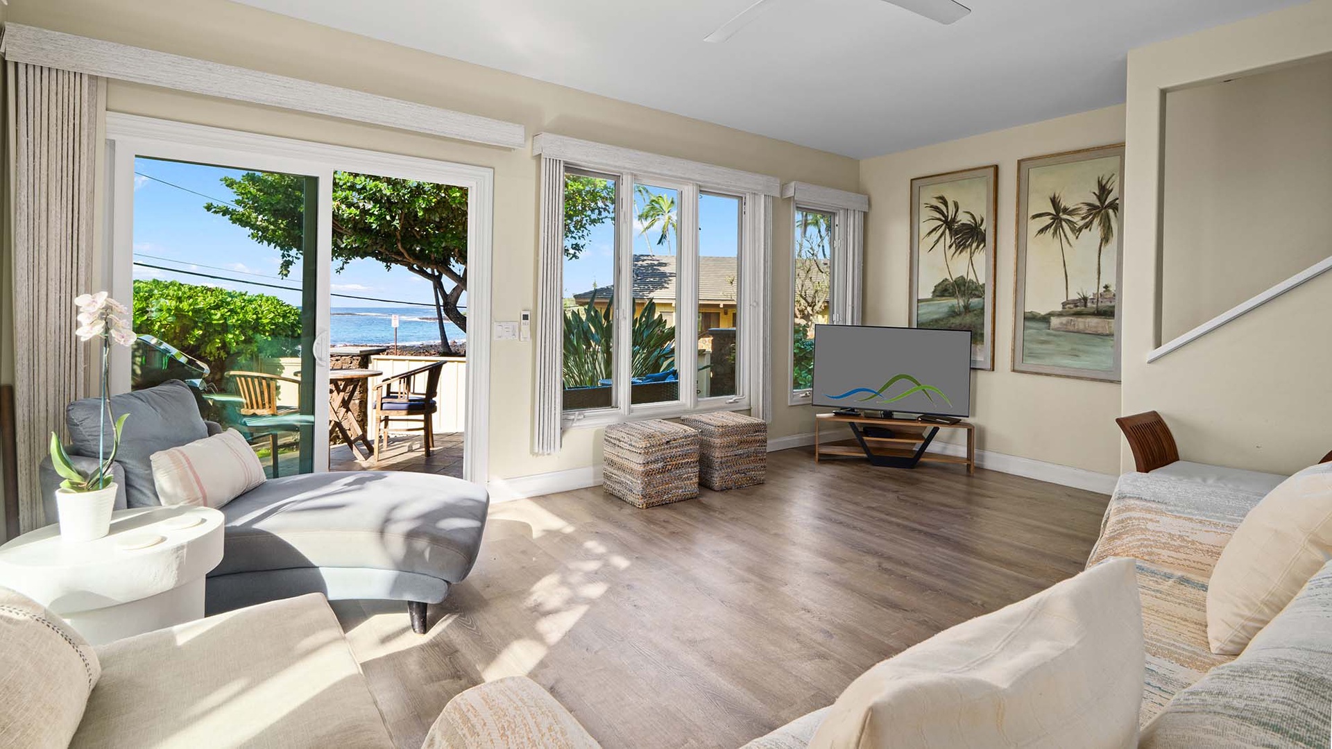 Your bright living room opens to a private patio with ocean views, featuring comfortable seating and tropical-themed artwork.