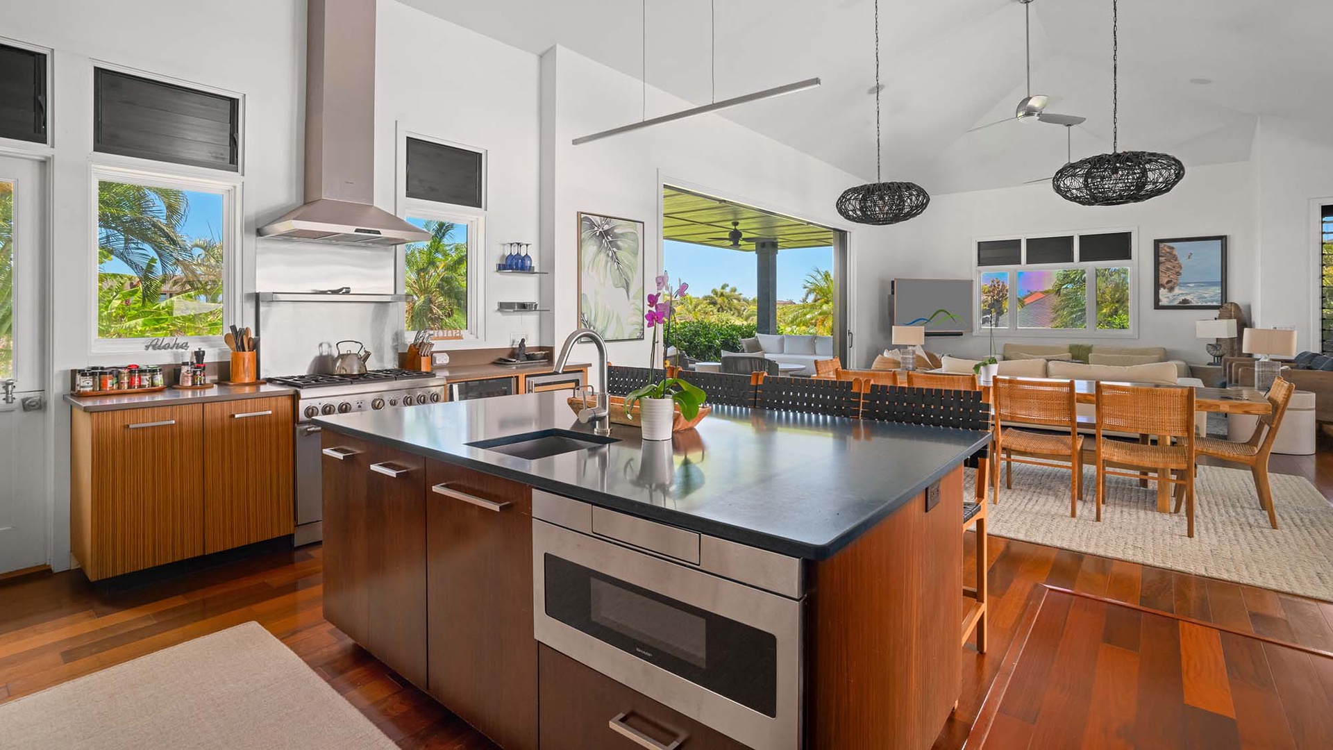 Step into your open-concept haven where a sleek kitchen flows into your dining space, framed by tropical views through floor-to-ceiling windows that invite the island breeze inside.