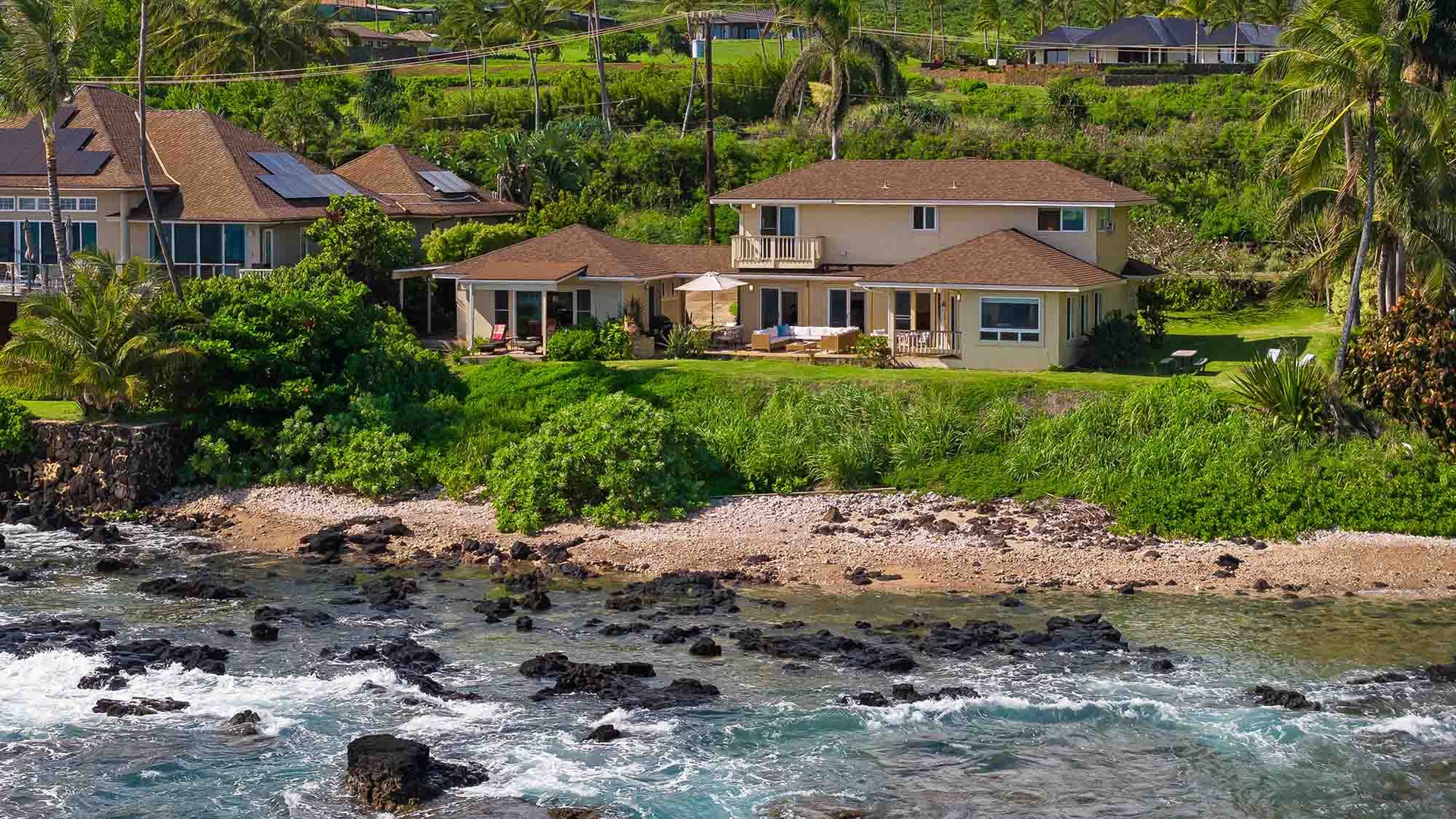 Waterfront property nestled in lush tropical landscaping with direct ocean access and expansive lawn areas, surrounded by swaying palms and neighboring homes.