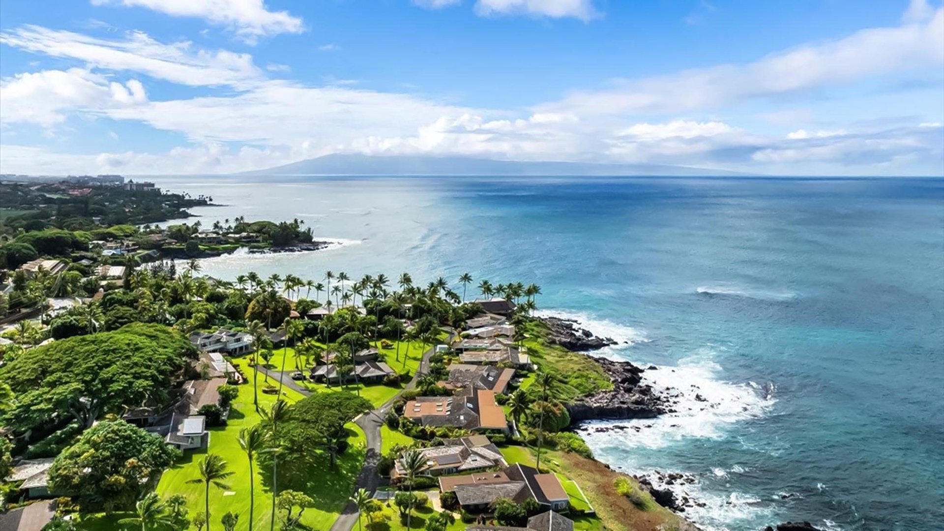 Stunning aerial view of tropical coastline with pristine blue waters, lush vegetation, and oceanfront properties nestled along dramatic cliffs.