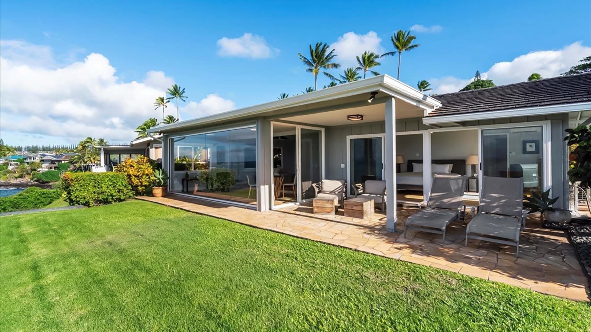 Modern beachfront villa with expansive lawn and tropical palm trees, featuring covered outdoor living spaces perfect for island relaxation.