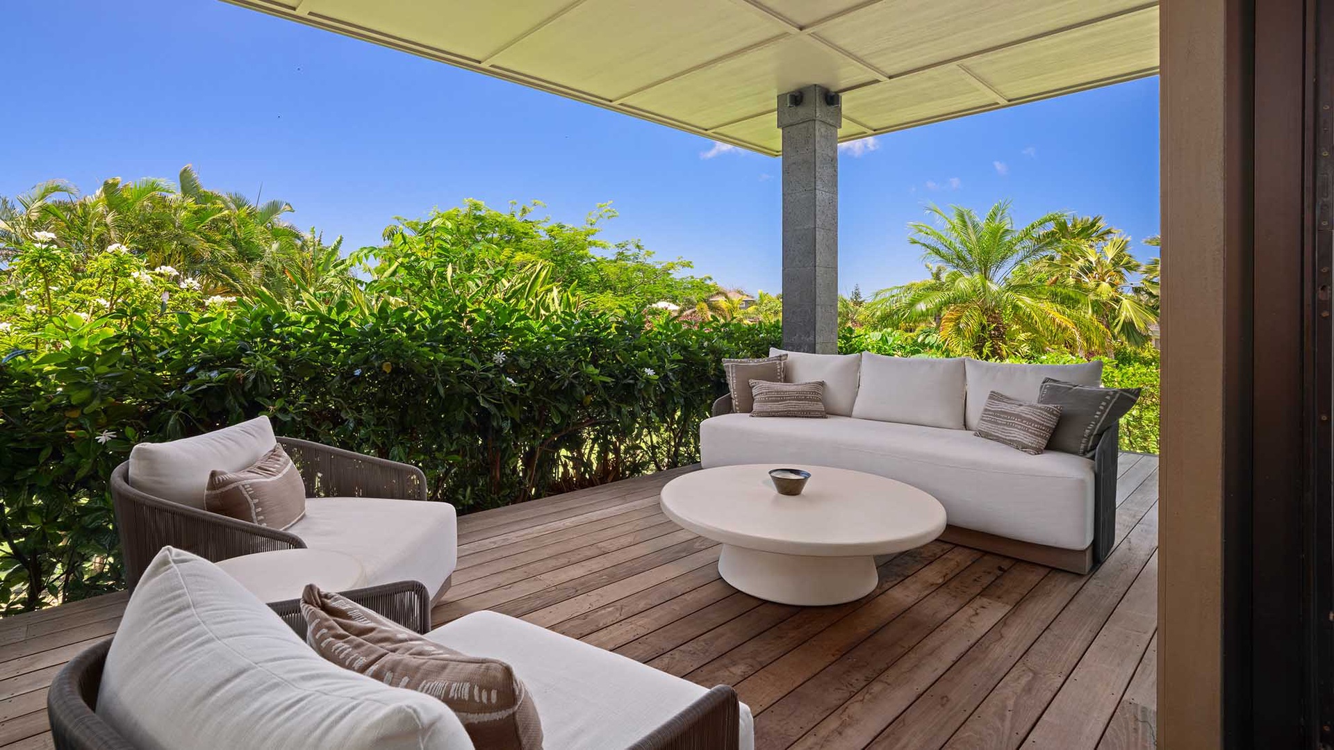 Your private terrace overlooks lush tropical greenery and palm trees, offering a serene outdoor retreat with plush lounging furniture and a breezy open-air design.