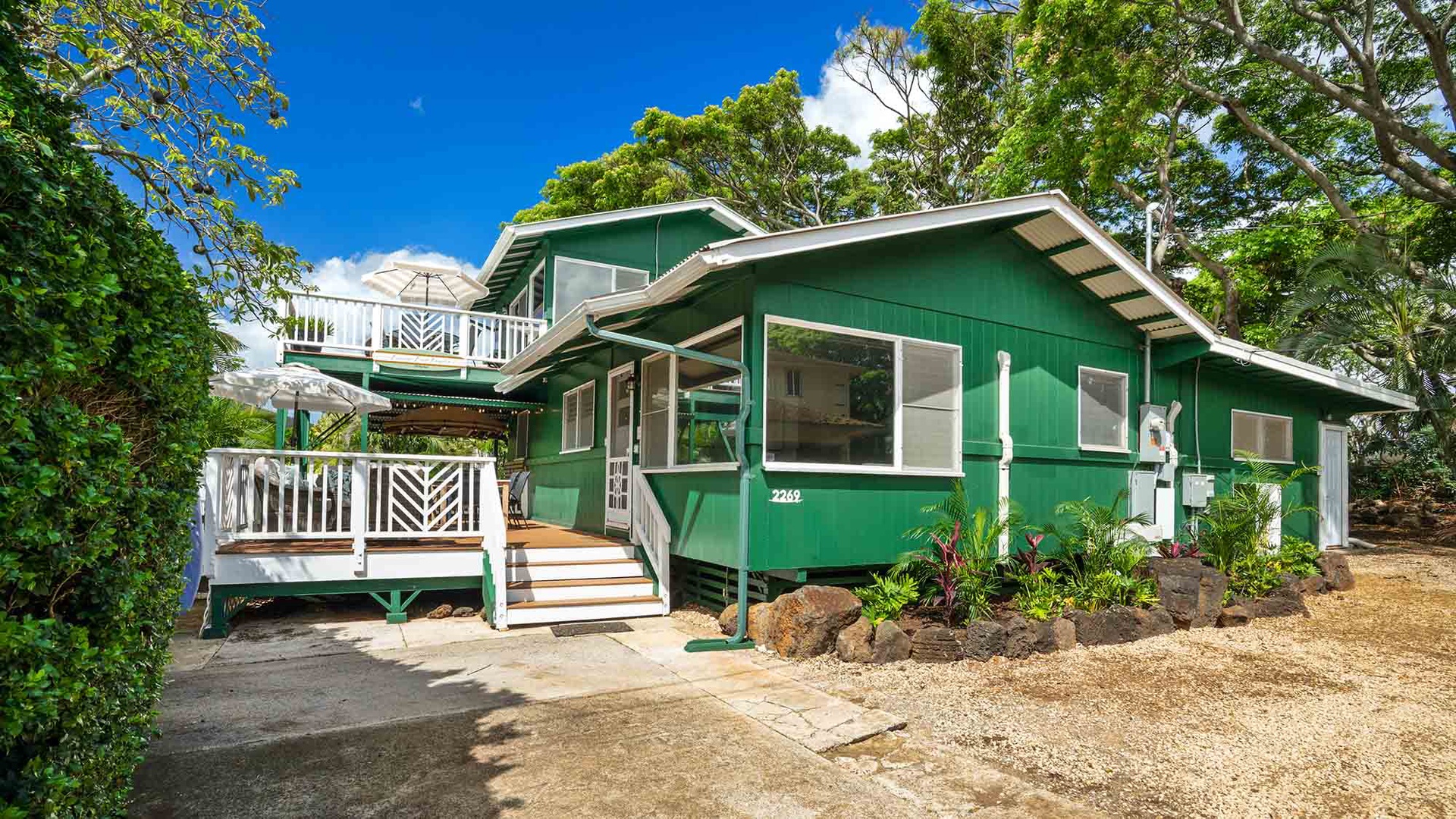 The distinctive green exterior and spacious deck welcome you to your tropical island retreat, surrounded by lush greenery and sunshine.