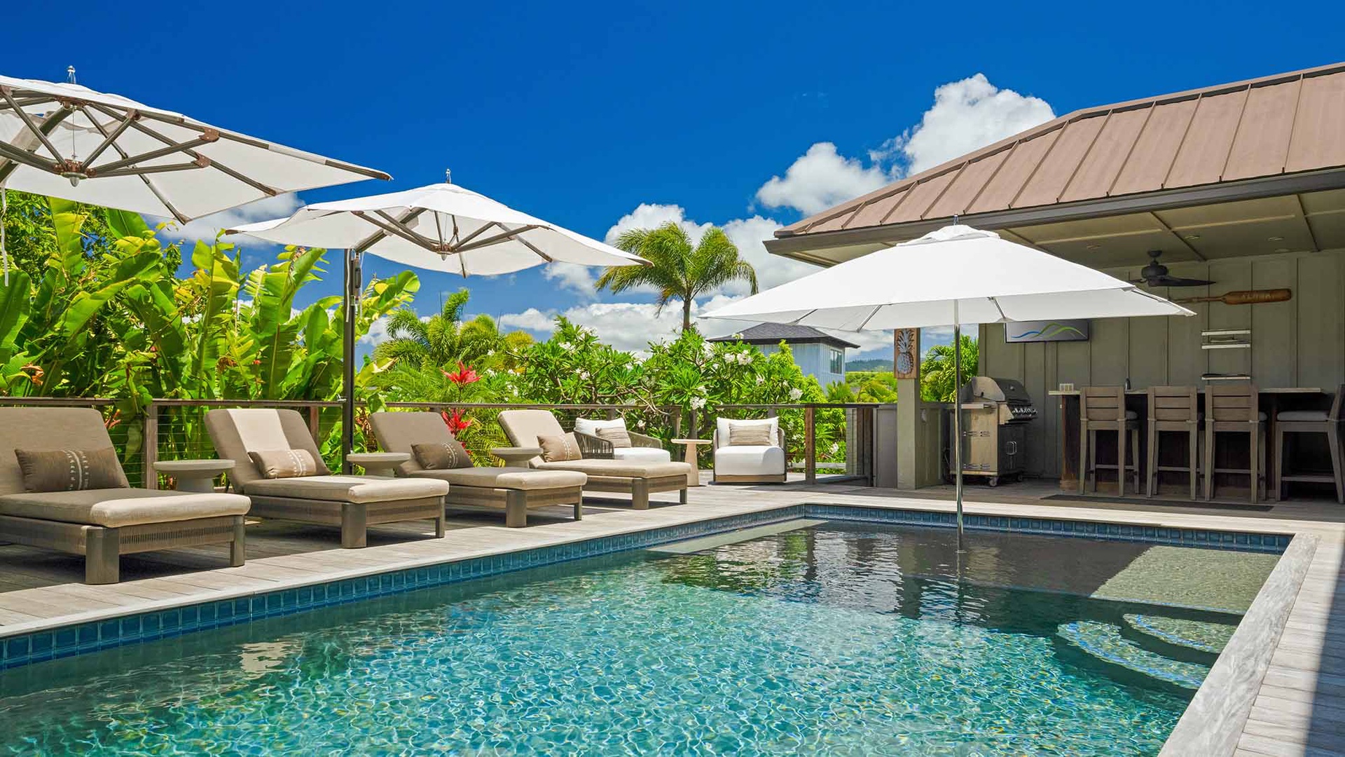 A serene private pool and modern covered bar area surrounded by lush tropical greenery create your perfect outdoor entertaining space under endless blue skies.