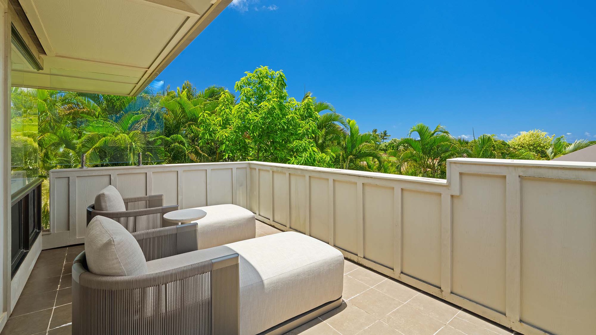 Step onto your private balcony, where plush seating awaits beneath lush tropical greenery and endless blue skies—perfect for morning coffee or evening relaxation.