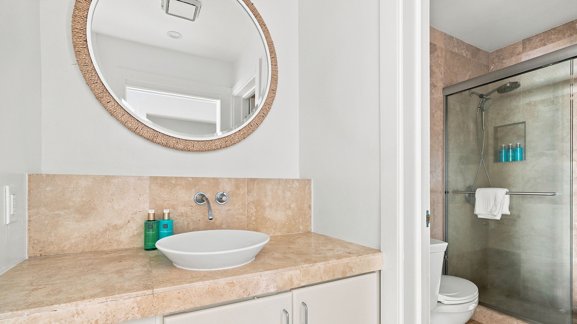 Step into your stylish bathroom with travertine finishes, a sleek vessel sink, and a rainfall shower—ready to refresh you after a day exploring paradise.