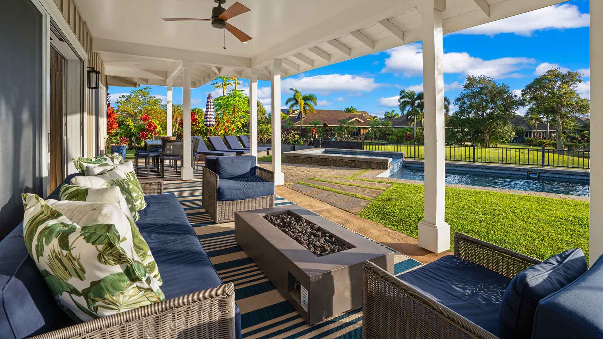 Tropical residential neighborhood with single-family homes, palm trees, manicured lawns, and a community pool, set beneath sunny skies and lush greenery.