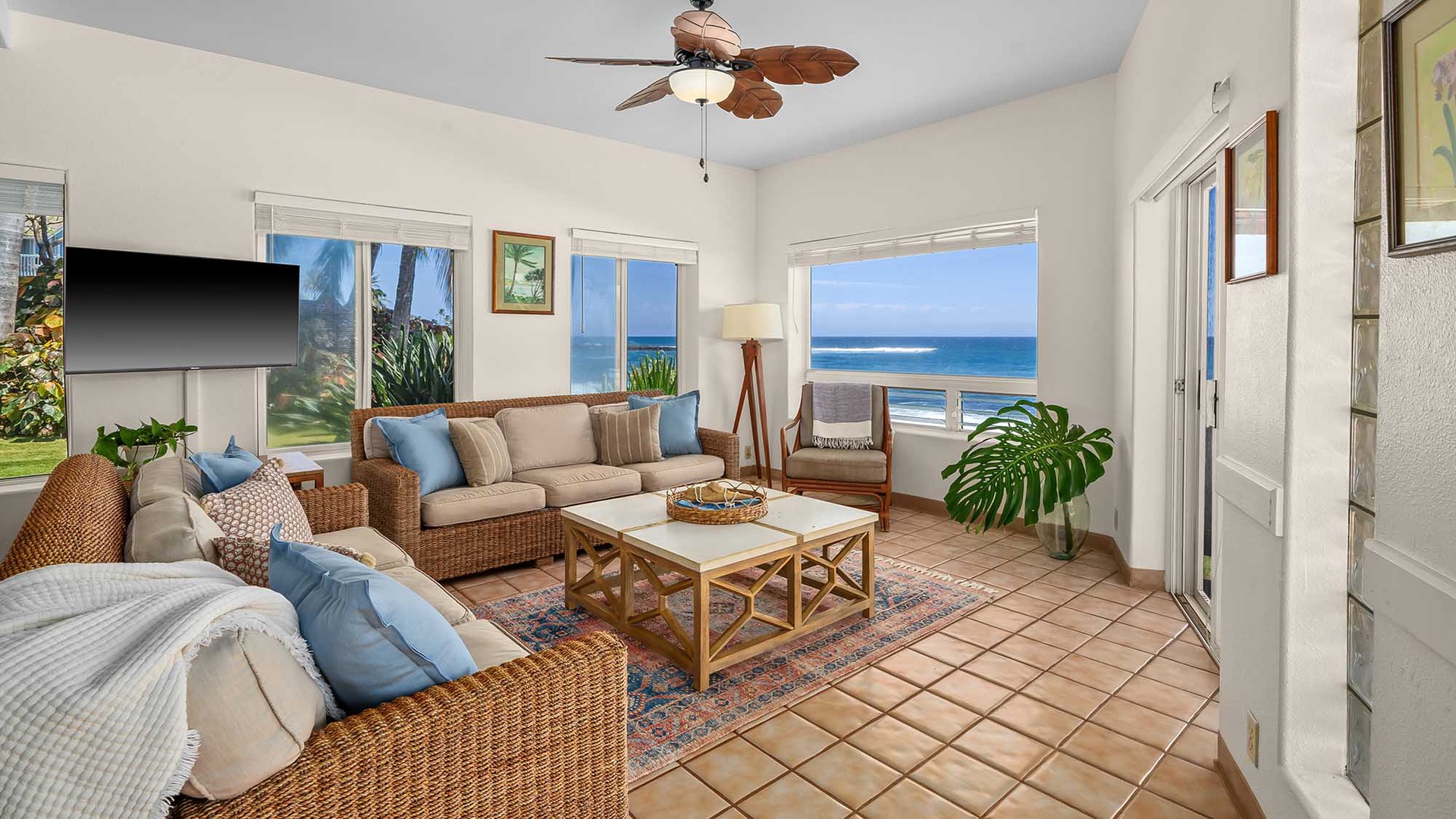 Sink into coastal comfort surrounded by woven textures and soothing blues—your oceanfront living room features floor-to-ceiling windows framing endless blue waters, inviting you to unwind with the sound of waves just beyond the glass.