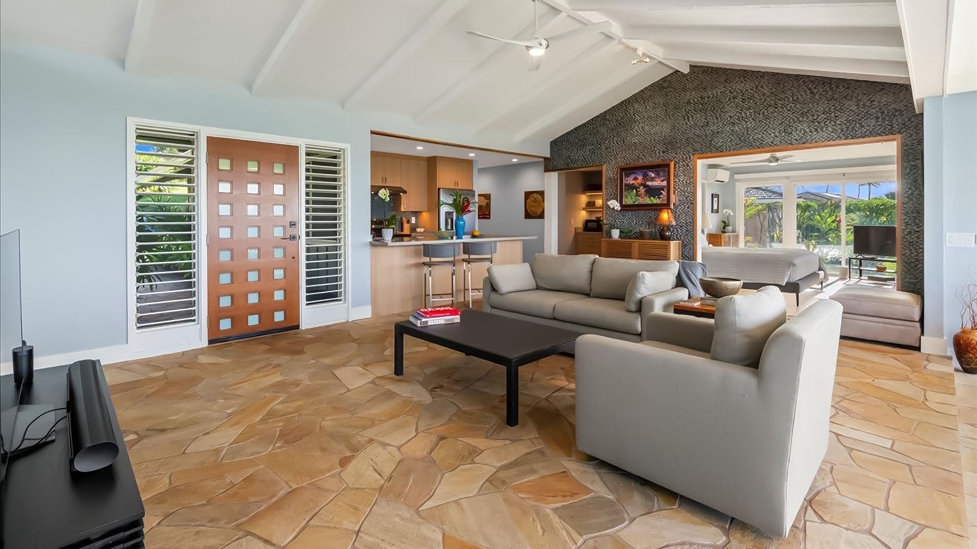 Unwind in your spacious open-plan living area with modern furnishings, natural stone floors, and tropical views through floor-to-ceiling windows.