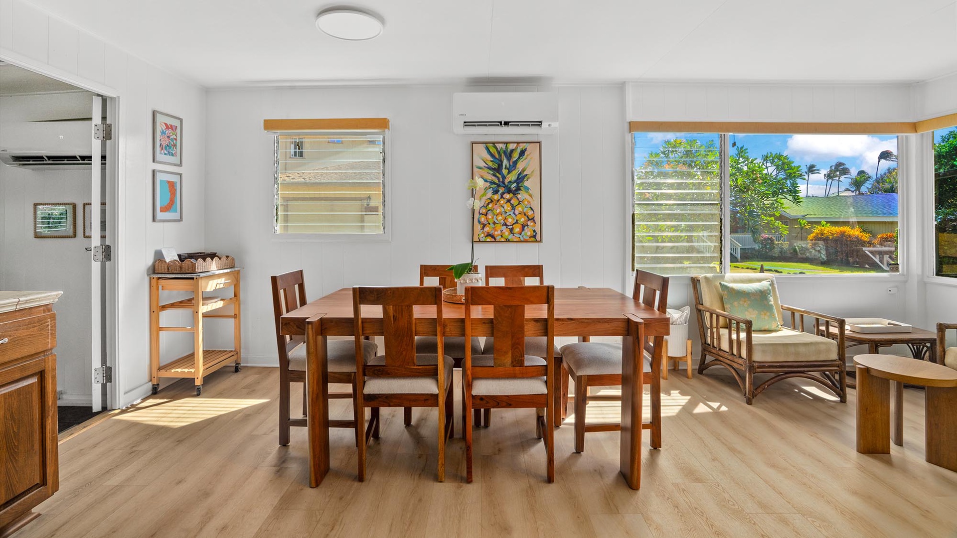 Gather around this spacious dining table where coastal charm meets island comfort. Large windows frame lush tropical views and warm sunlight floods the room, creating the perfect setting for leisurely meals with your group.