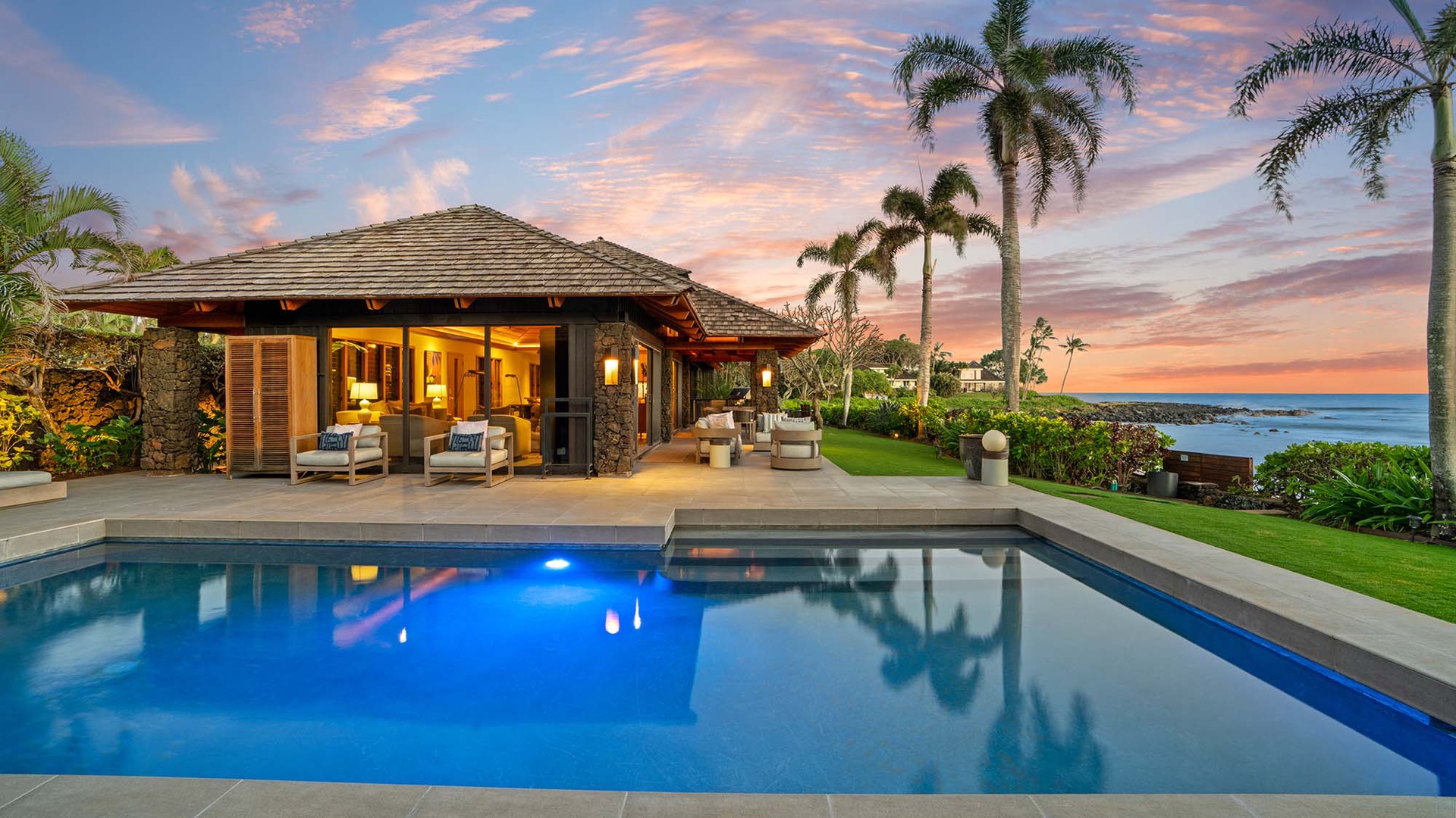 Tropical villa with infinity pool overlooking the ocean, surrounded by swaying palms under a stunning sunset sky.