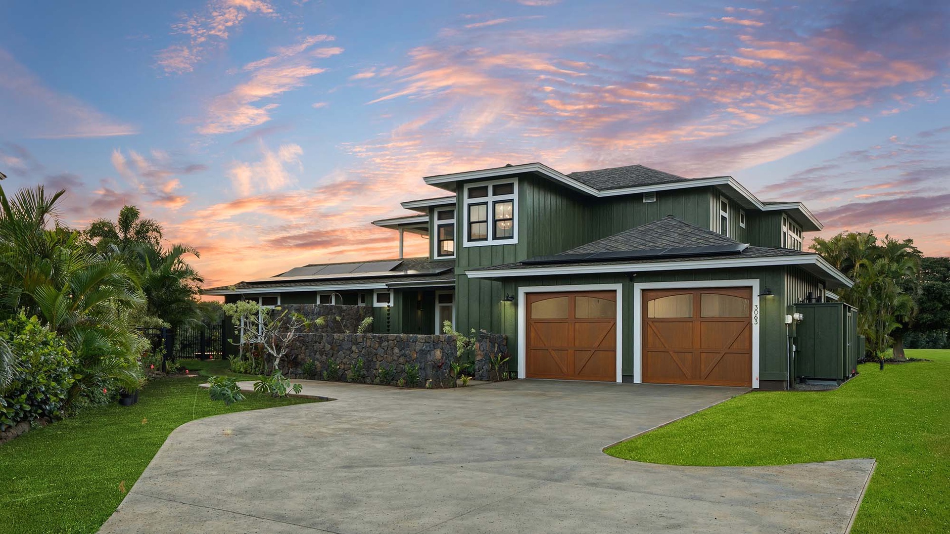 Modern tropical home with stunning sunset sky backdrop, surrounded by lush palm trees and manicured lawns.