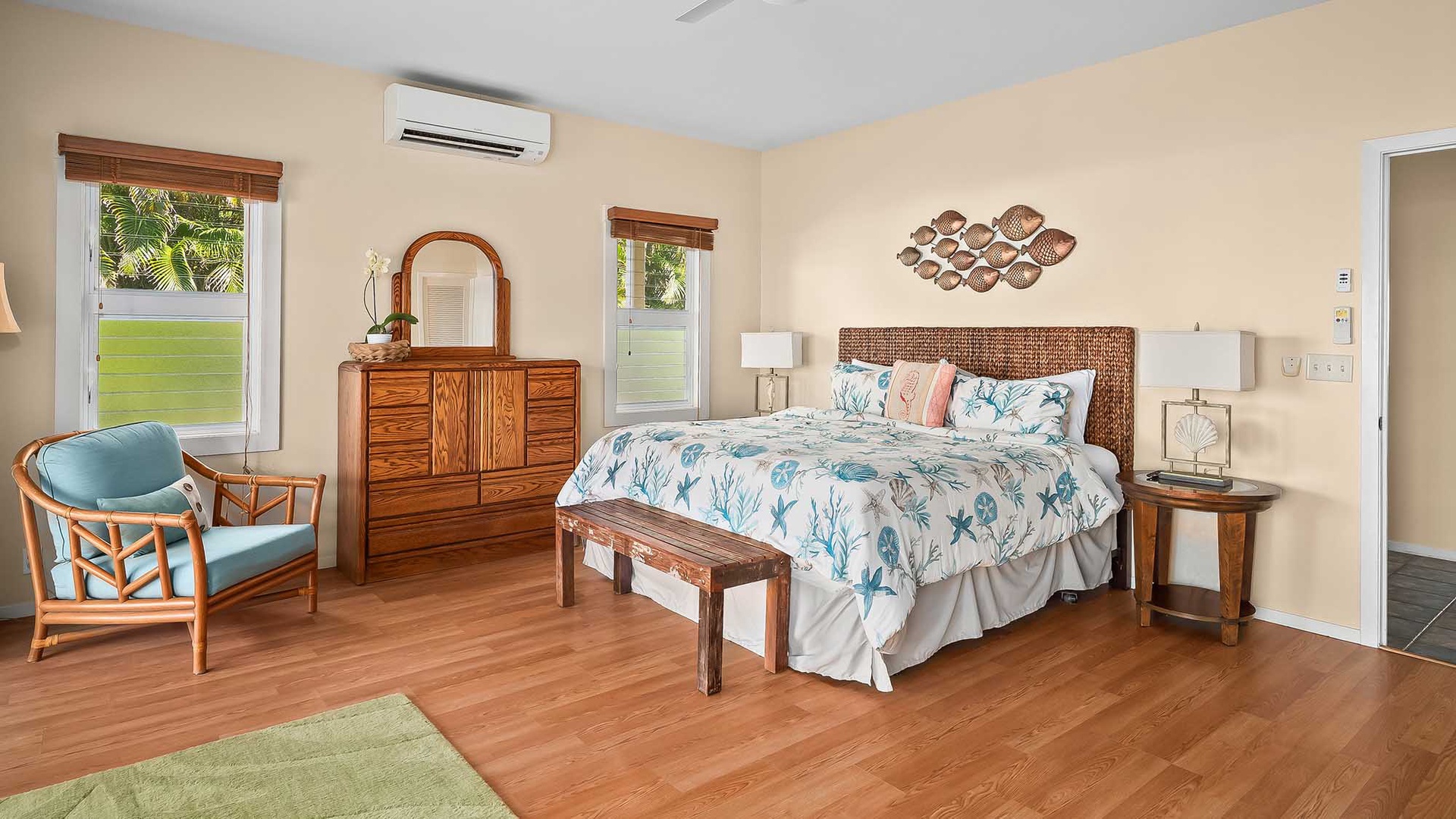 Your coastal-inspired bedroom features a woven headboard, tropical bedding, and warm hardwood floors, with air conditioning keeping you comfortable under the peaceful island breeze outside.